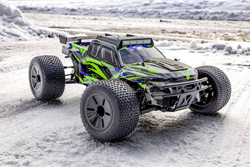 Een afstandsbediend, vierwielaangedreven auto met een groen-zwart design staat op een met sneeuw bedekte weg.