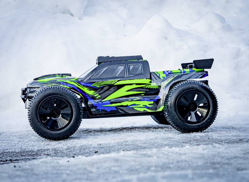 Een afstandsbediend autootje met groene en blauwe patronen staat op een met sneeuw bedekte ondergrond.