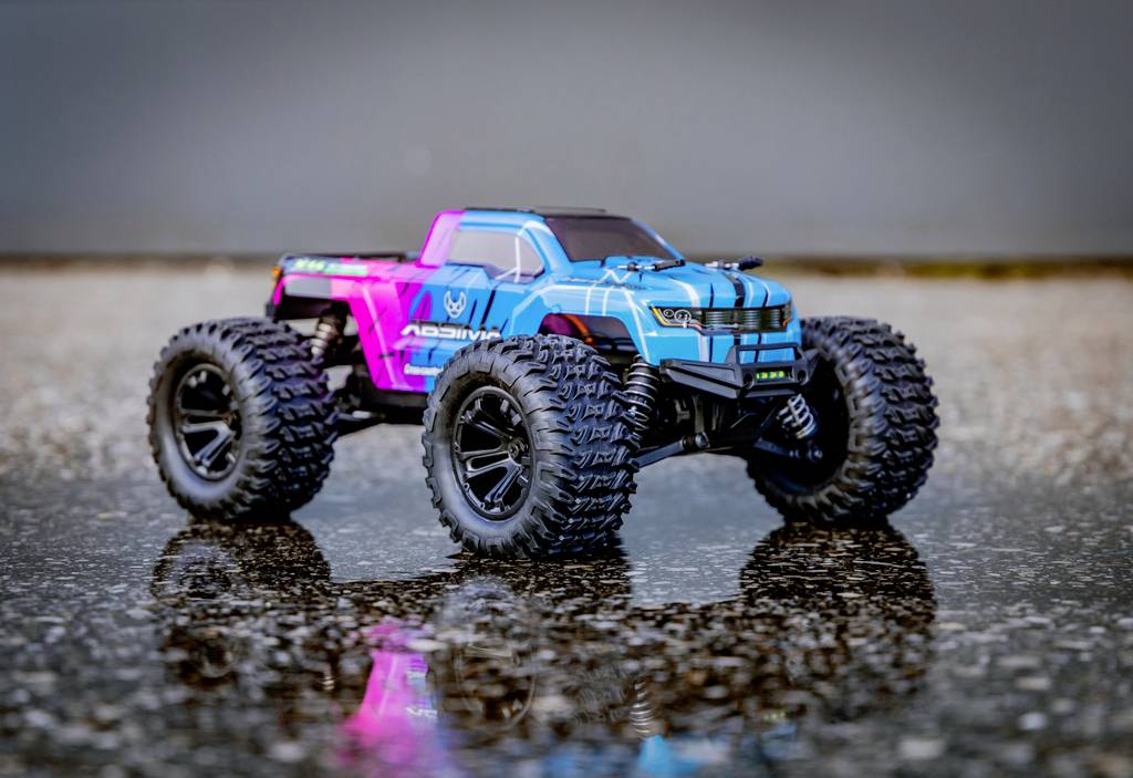 Speelgoed-monstertruck in blauw en roze weerspiegeld op nat asfalt. Grove banden, moderne carrosserie, dynamisch design.