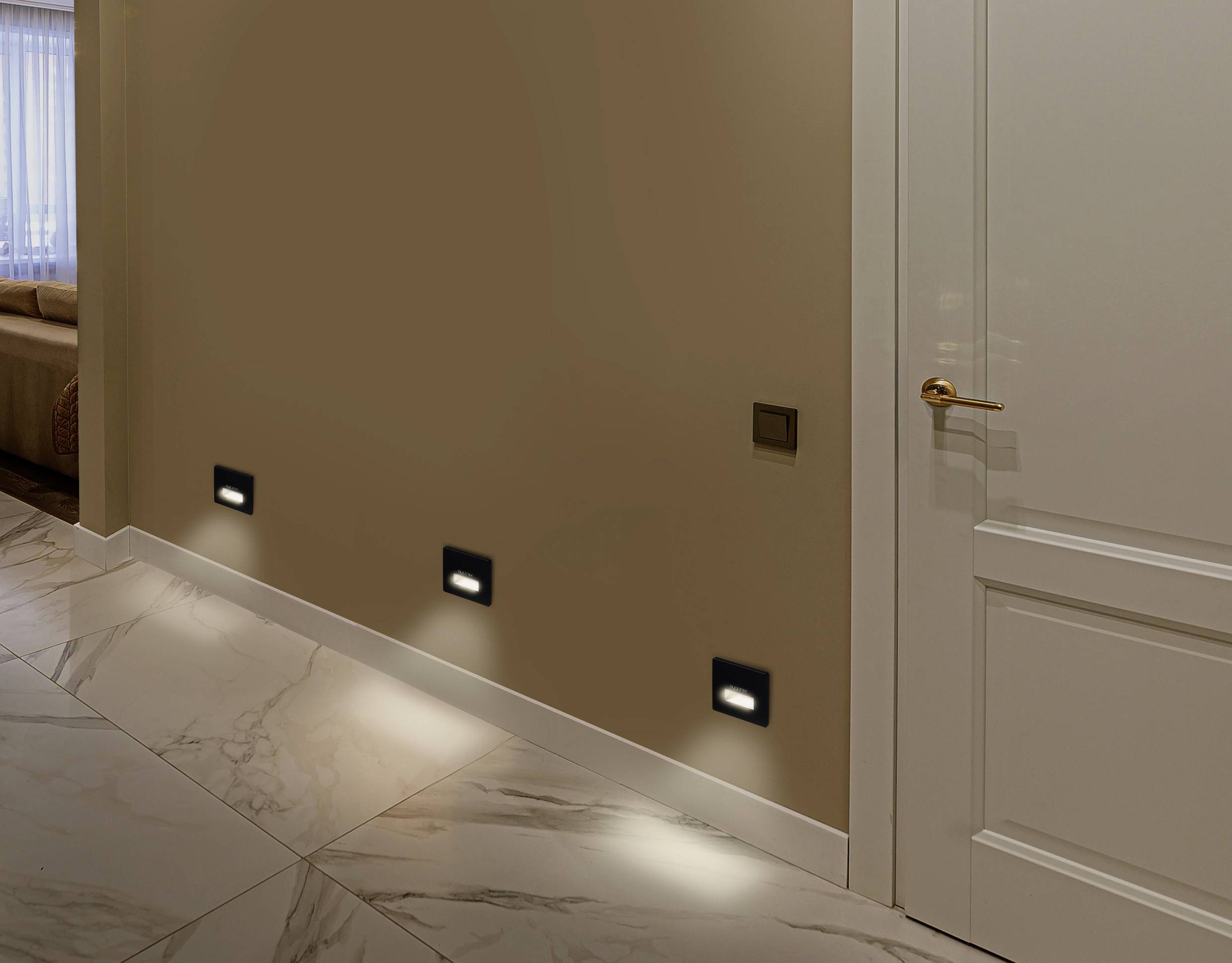 Verlichte gang met moderne wandlampen die zacht licht werpen op de witte marmeren vloer. Een open deur leidt naar een andere ruimte.
