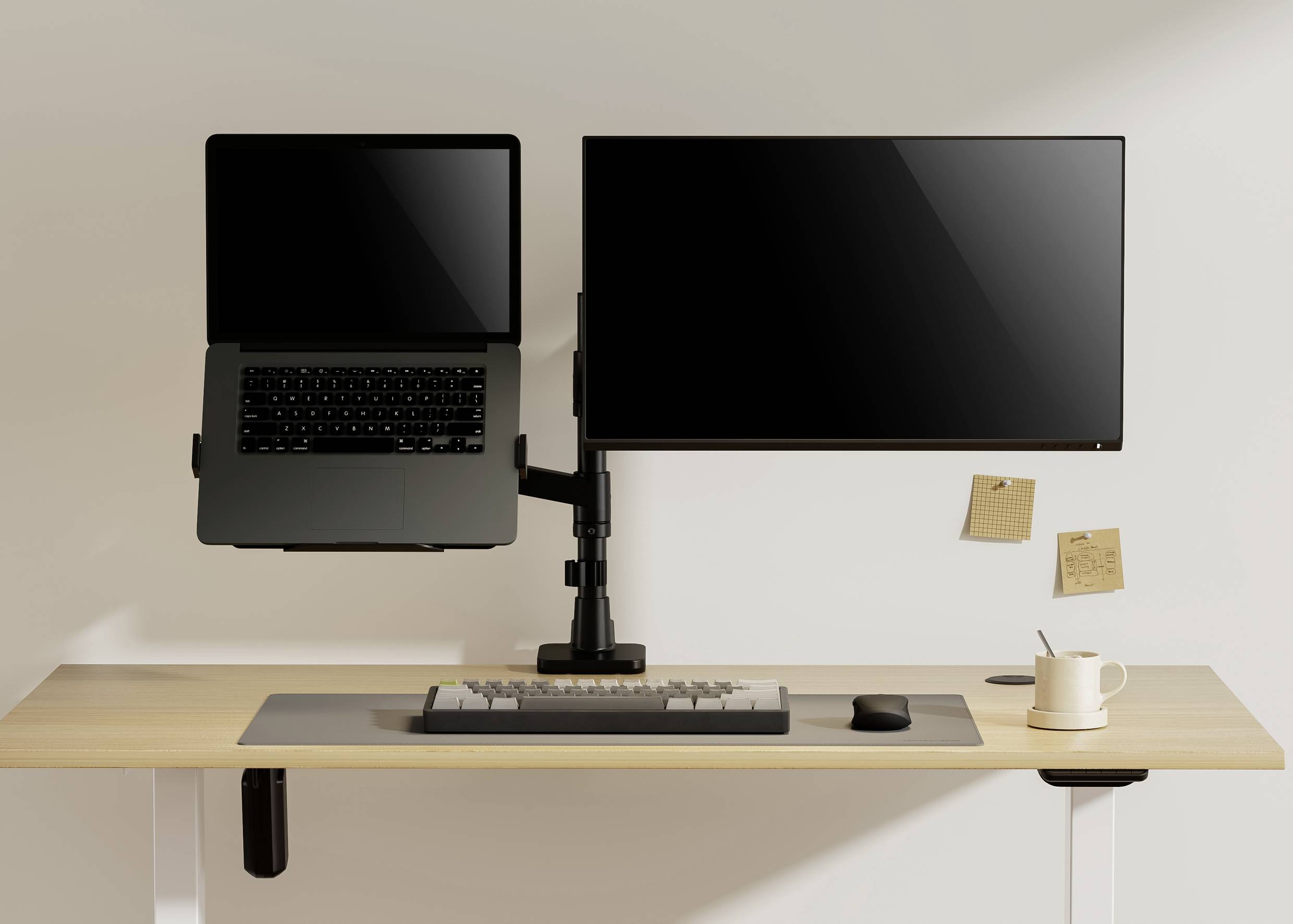 Een bureau met een laptop en een externe monitor op monitorarmen. Eronder een toetsenbord, een muis en een mok.