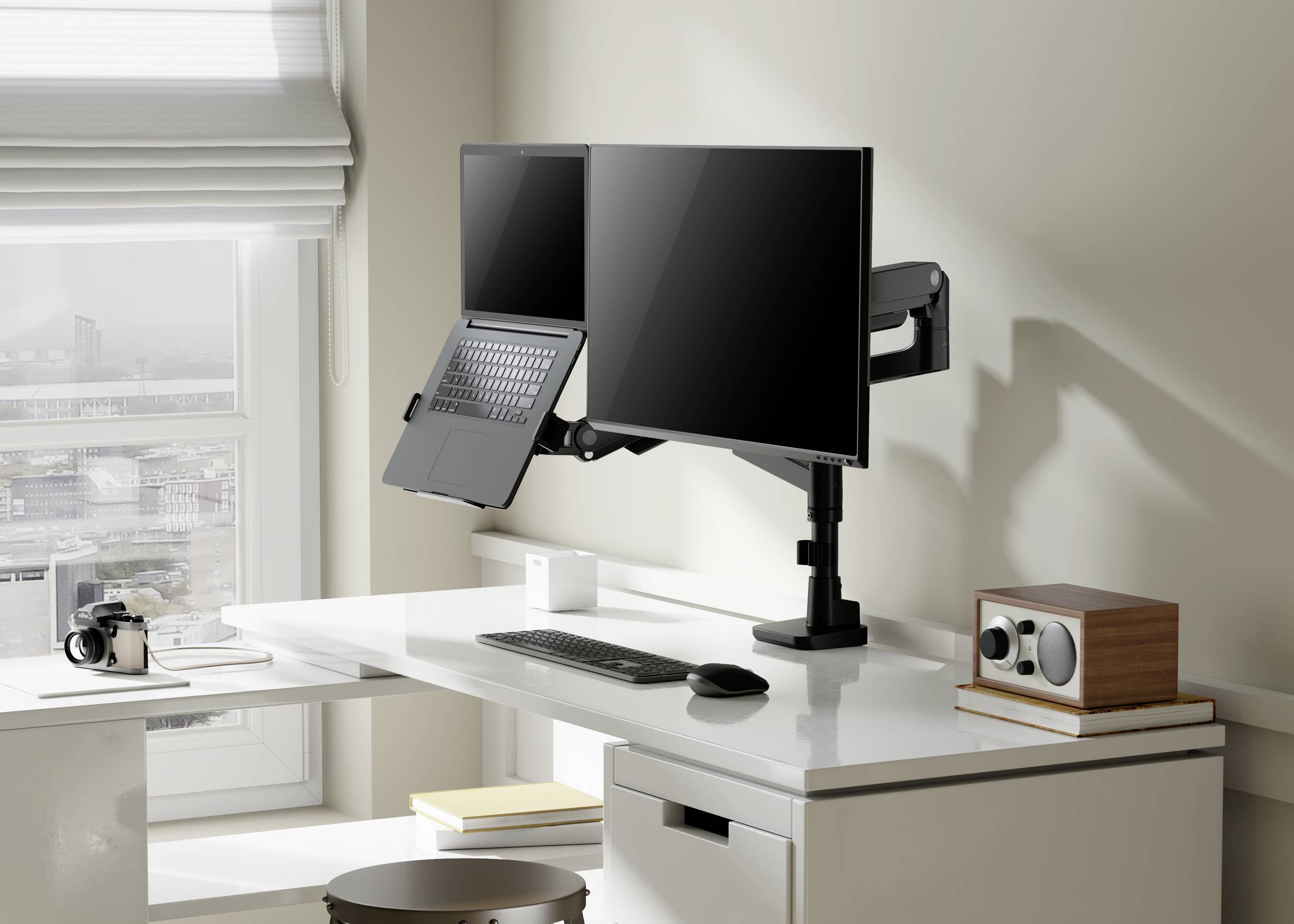 Een moderne, opgeruimde bureau met twee monitoren, een laptop, toetsenbord, muis en een camera nabij het raam.