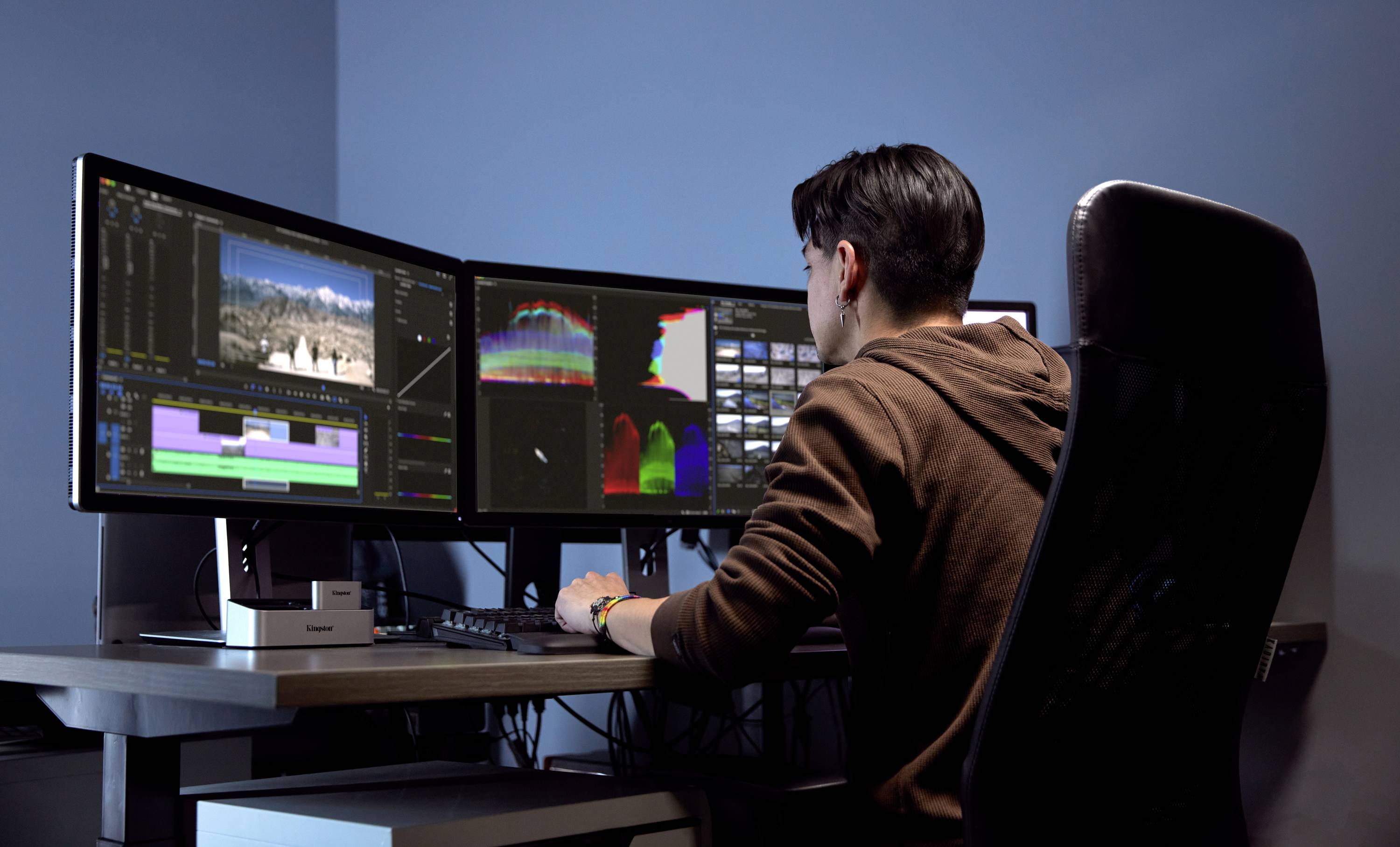 Een persoon werkt aan een computer met drie beeldschermen waarop video- en fotobewerkingsprogramma's worden weergegeven.