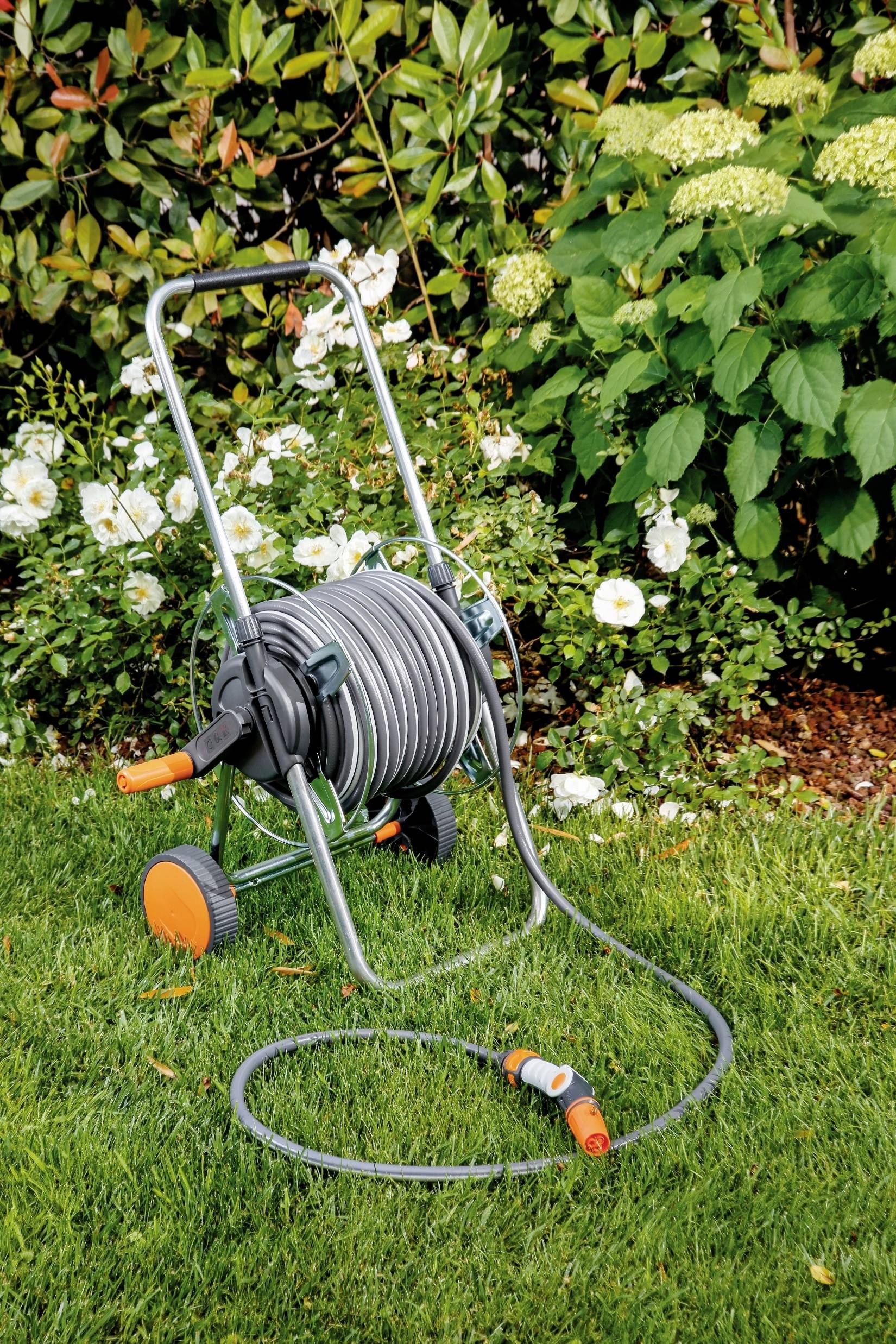 Tuinslangwagen op groen gras voor bloeiende struiken, klaar om te bewateren.