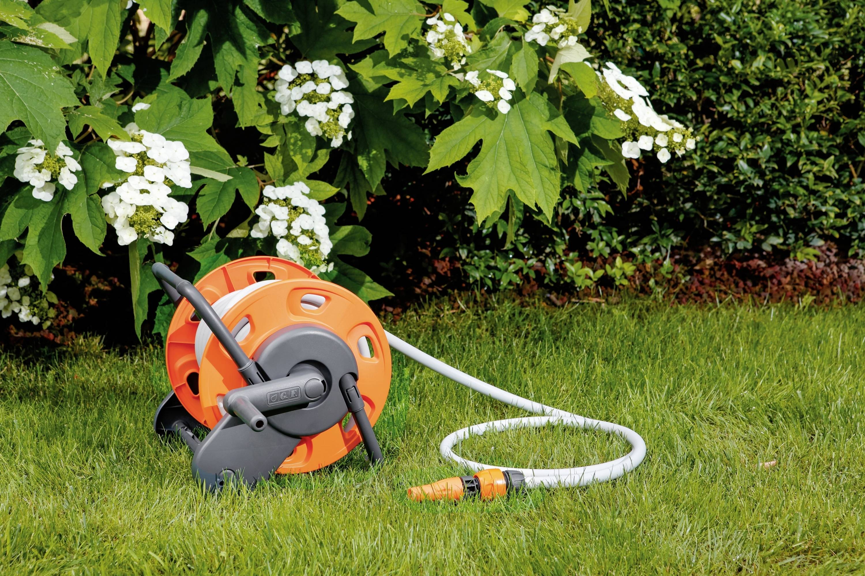 Slang op een oranje slanghaspel ligt op groen gras voor bloeiende witte hortensia's. Geschikt voor tuinberegening.