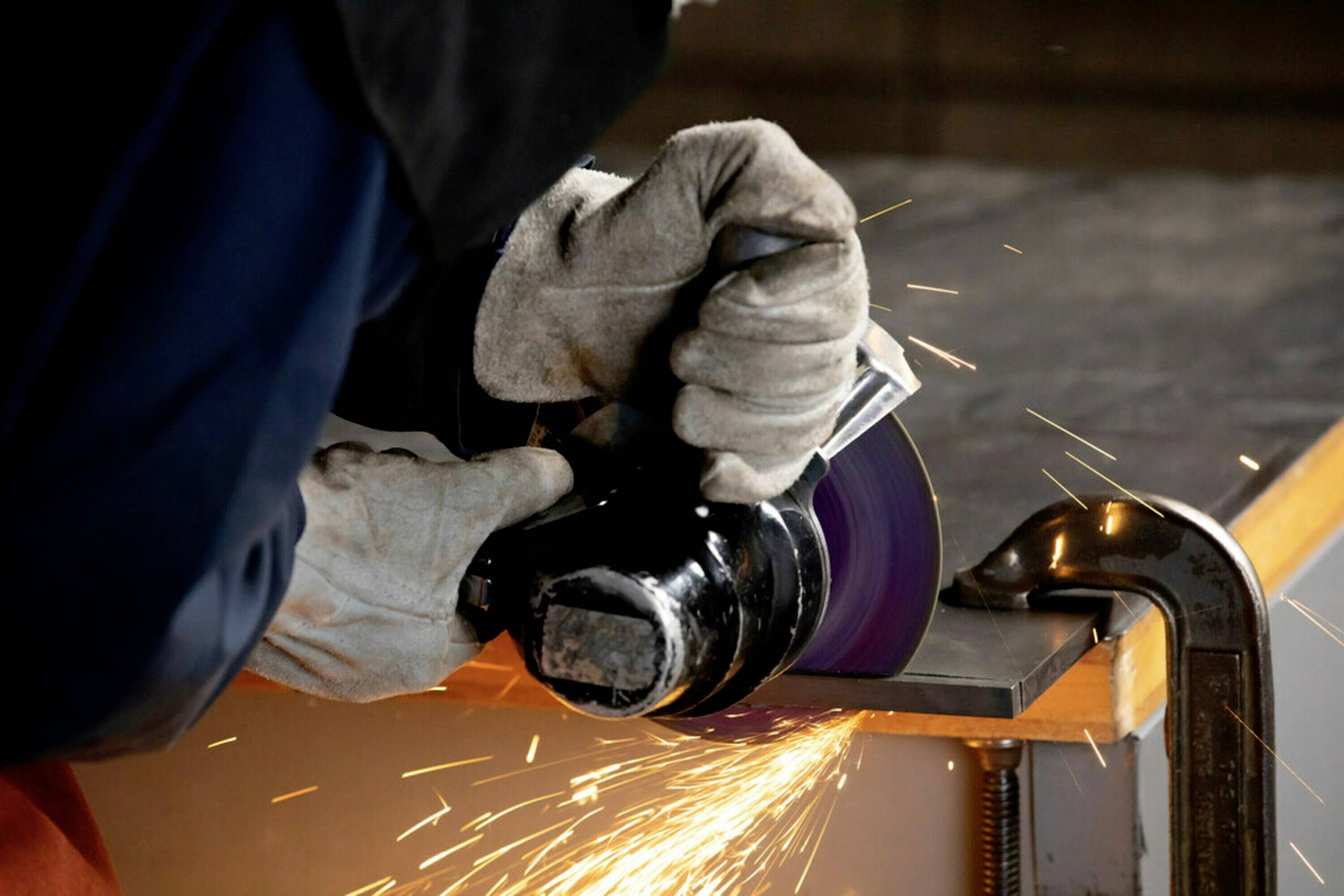 Een persoon slijpt een metalen rand met een haakse slijper, vonken spatten. Hij draagt beschermende handschoenen.