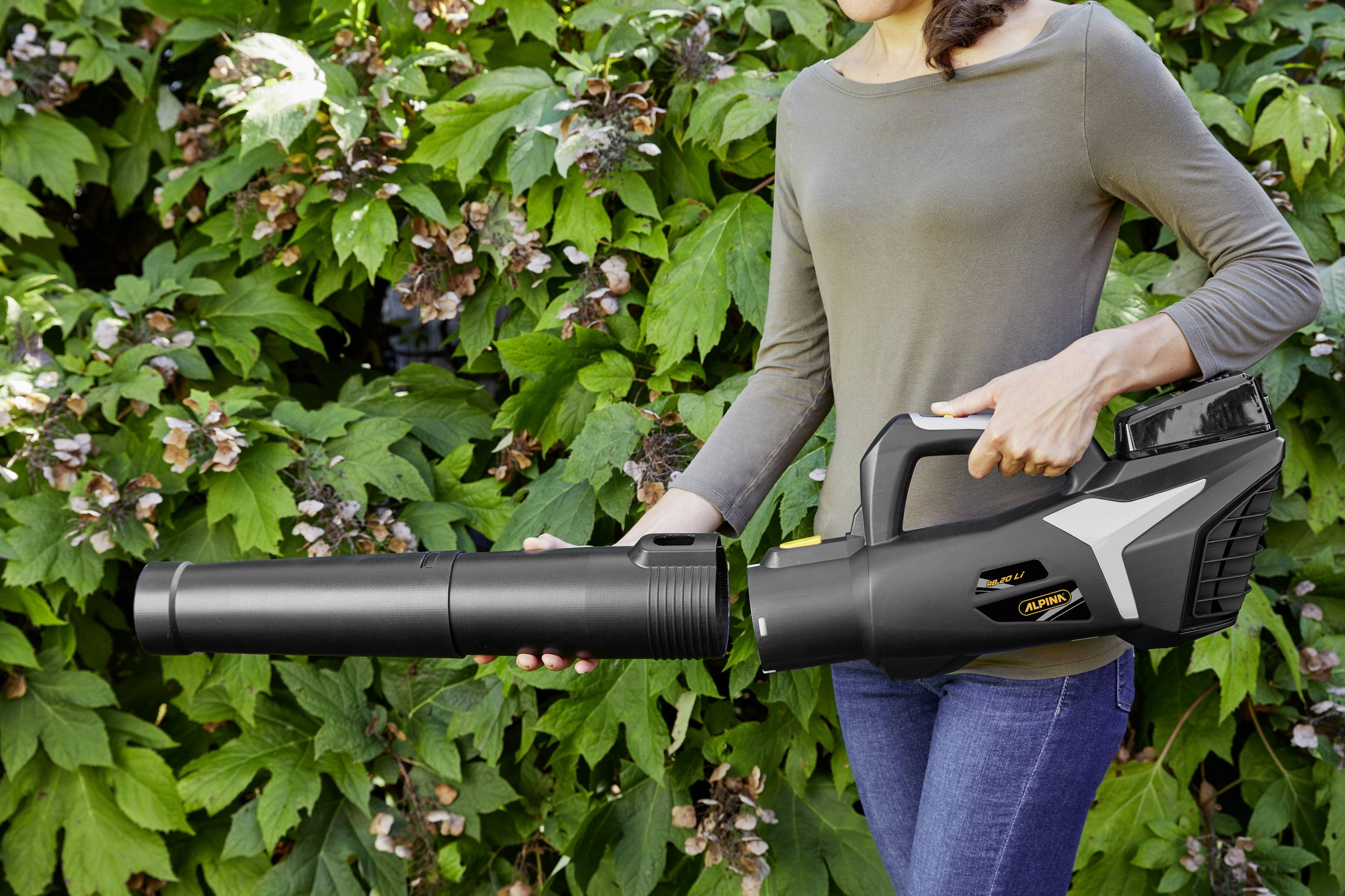 Een vrouw houdt een bladblazer voor een achtergrond van groene bladeren.