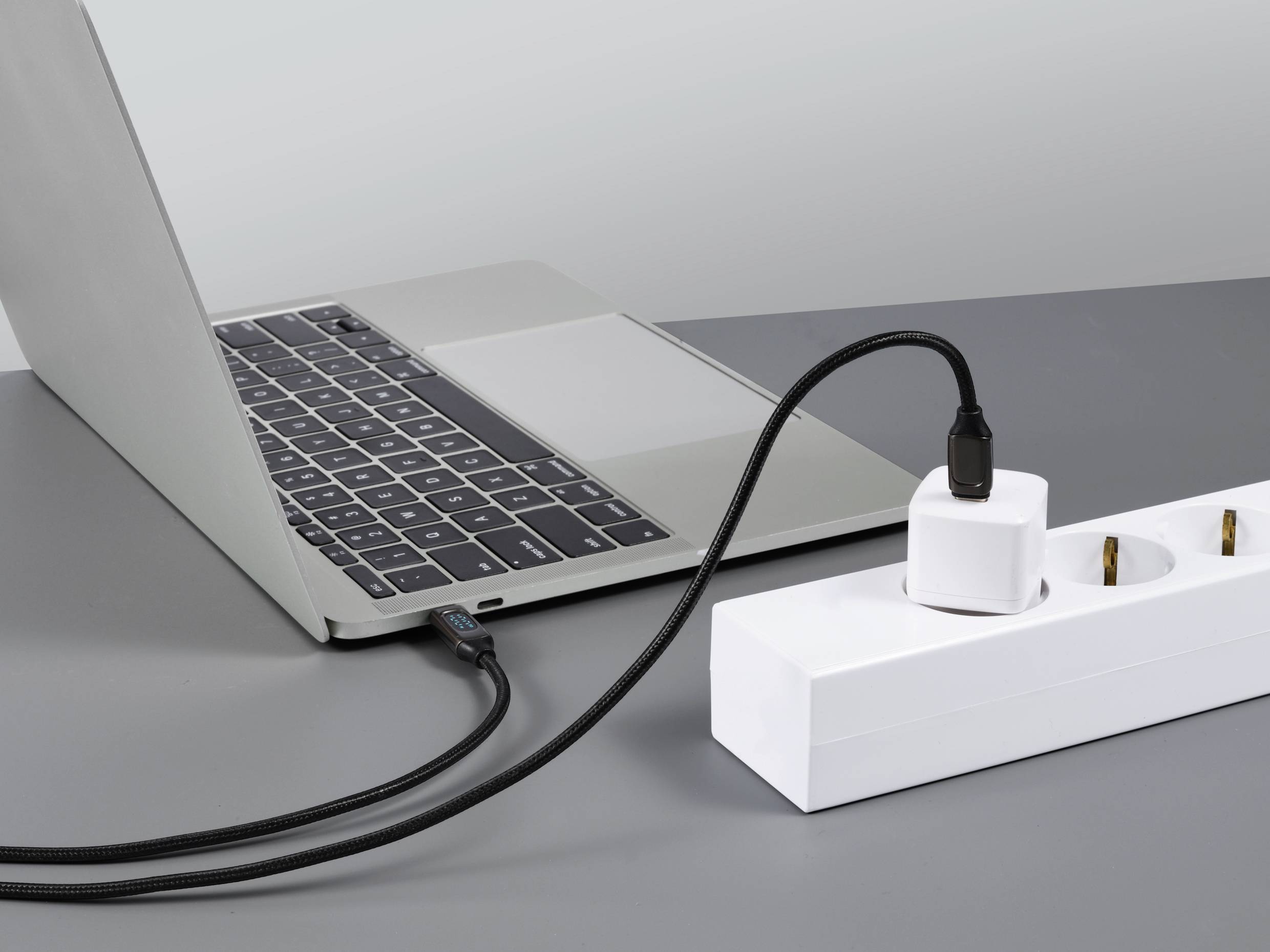 Een laptop is via een USB-kabel met een adapter aangesloten op een stekkerdoos en wordt opgeladen.
