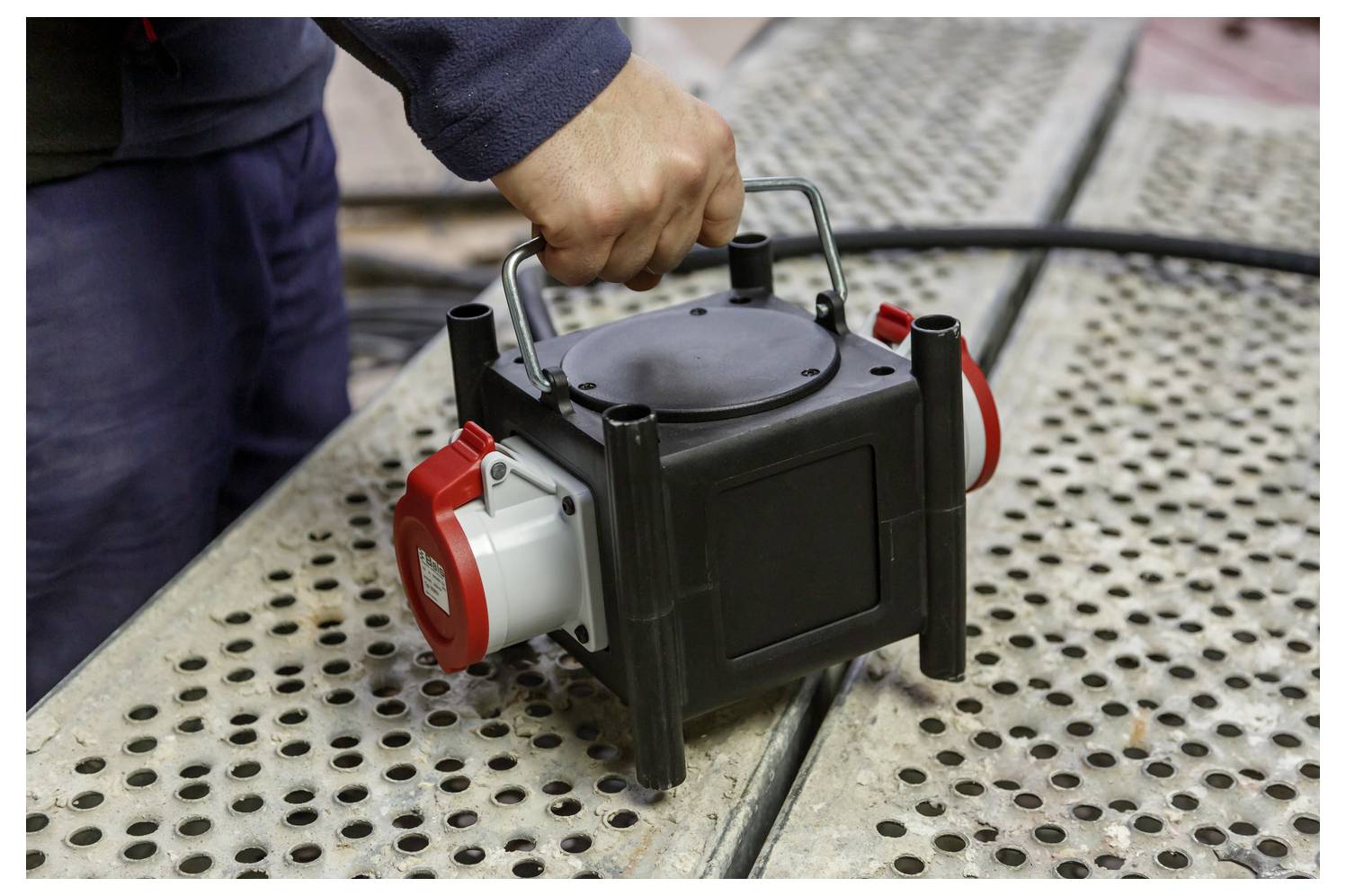 Hand die een draagbare elektrische pomp of generator op een geperforeerd metalen oppervlak buitenshuis vasthoudt.