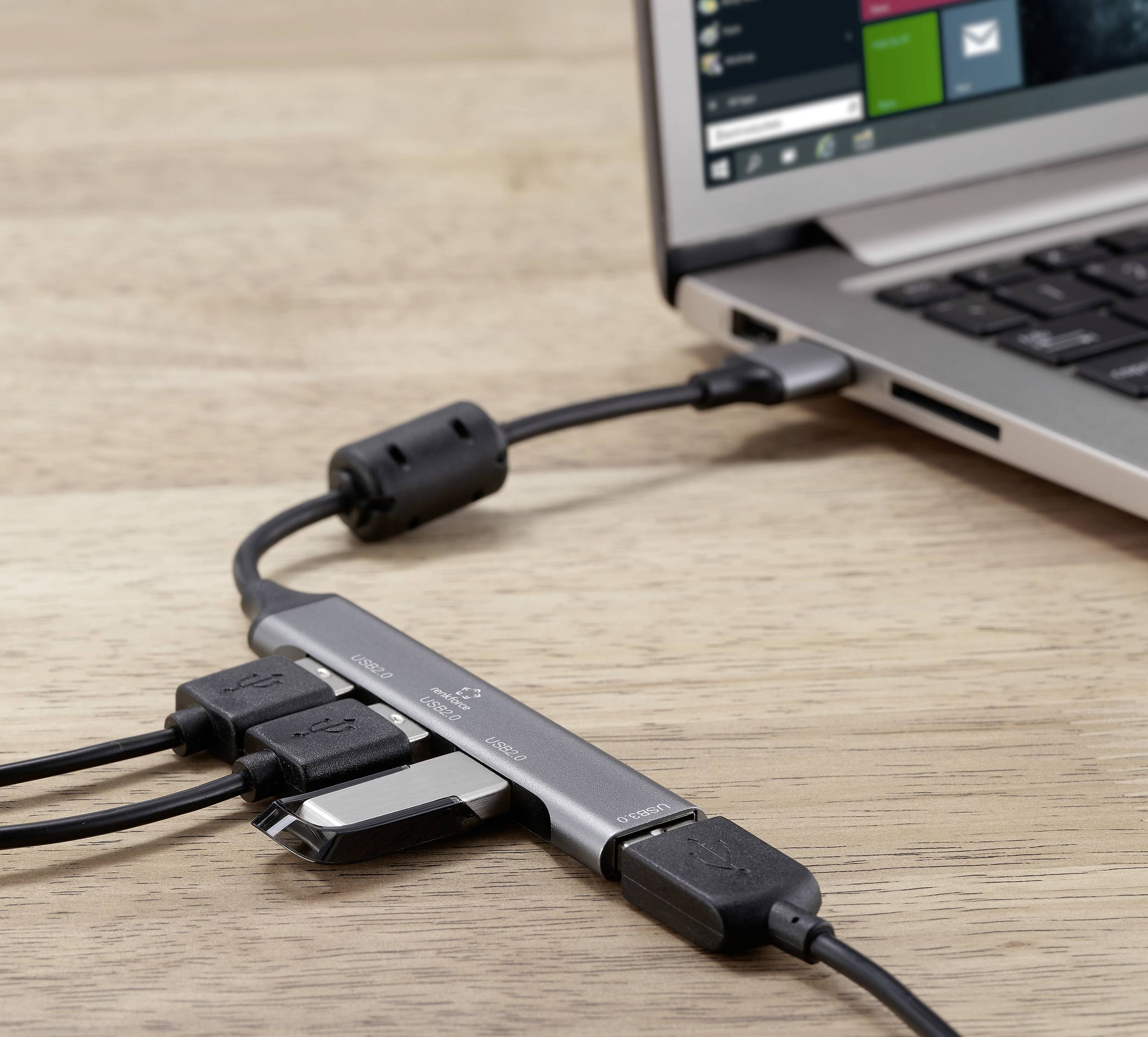 Een laptop is verbonden met meerdere USB-apparaten via een USB-hub. De hub ligt op een houten tafel, de laptop is gedeeltelijk zichtbaar.