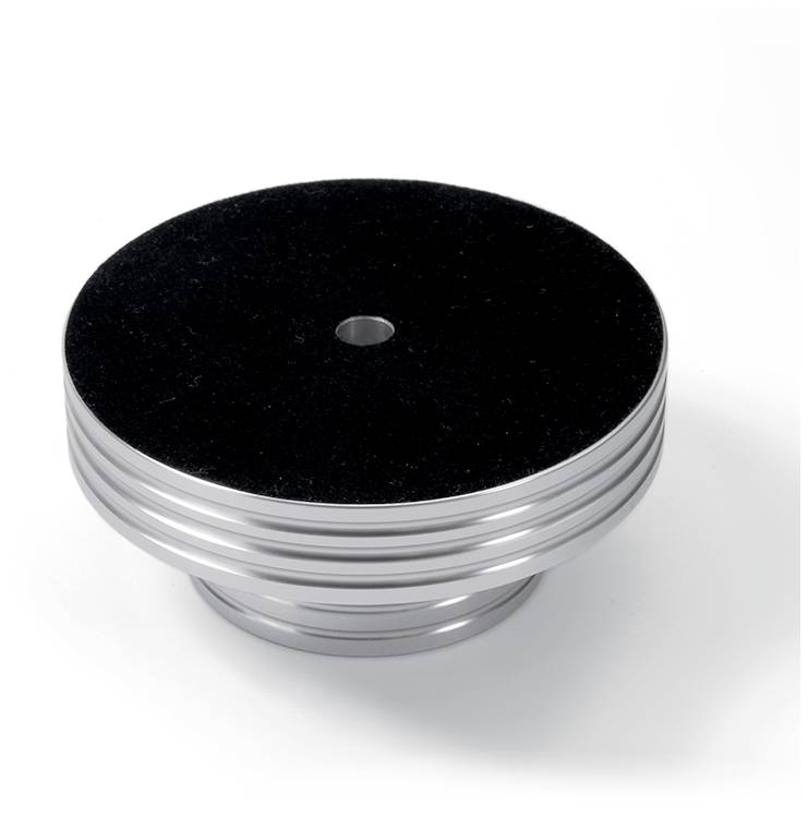 Een zilveren, rond metalen voorwerp met een zwarte, fluwelen bovenkant en een gat in het midden, op een witte ondergrond.