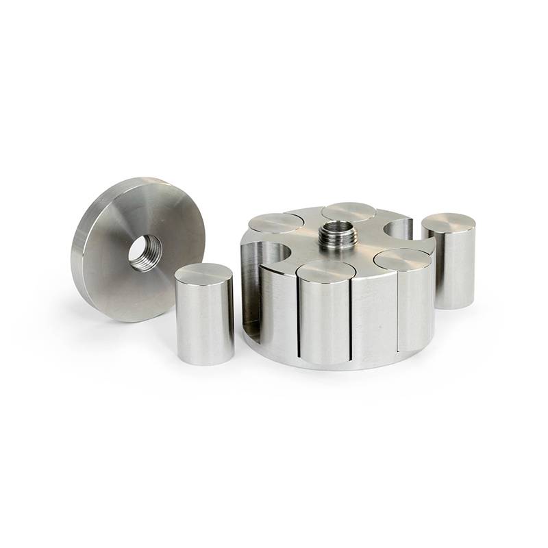 Een cilindrische metalen adapter met een schroefdraad, omringd door zes even grote cilindrische metalen onderdelen op een wit oppervlak.