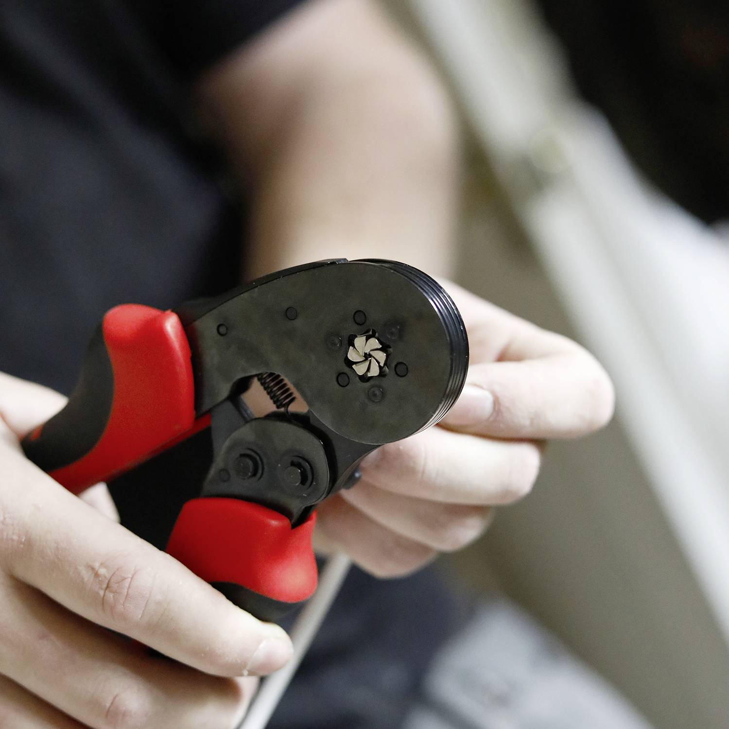 Een persoon bedient een rode en zwarte krimptang om een kabel te bewerken. De scène toont een close-up van de handen tijdens het werk.