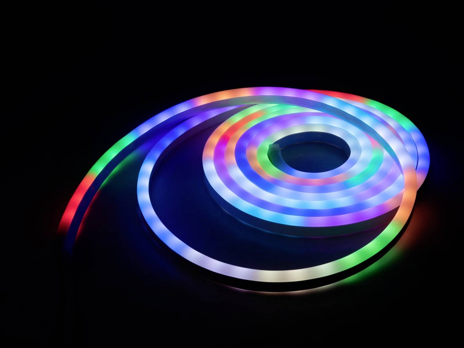 Een RGB-led-lichtstrip die in een spiraal is gewonden, licht op in meerdere kleuren, waaronder blauw, groen en rood, op een zwarte achtergrond.