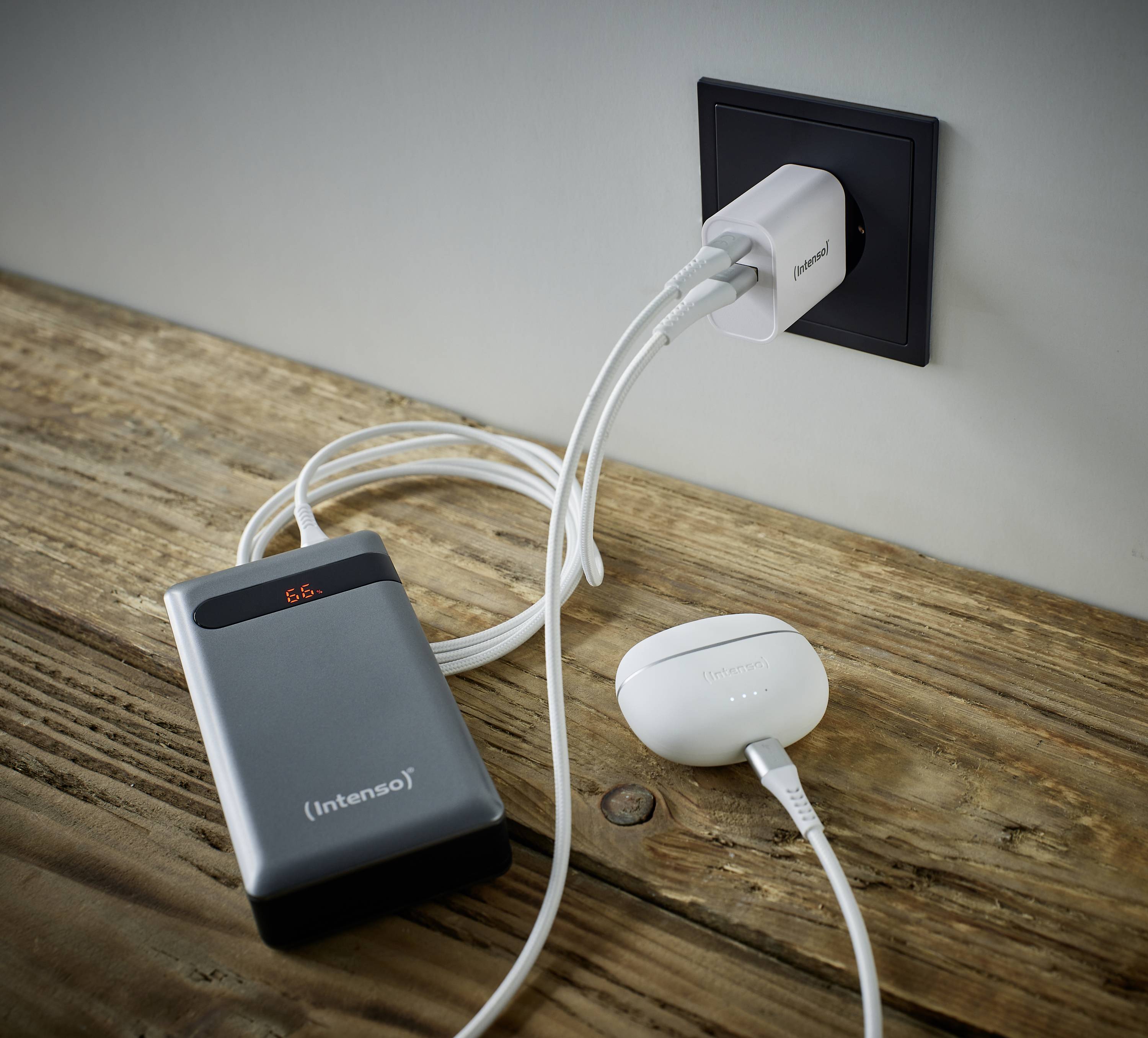 Een grijze powerbank en een witte adapter liggen op een houten tafel. Beide apparaten zijn via kabels aangesloten op een stopcontact.