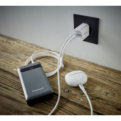 Een grijze powerbank en een witte adapter liggen op een houten tafel. Beide apparaten zijn via kabels aangesloten op een stopcontact.