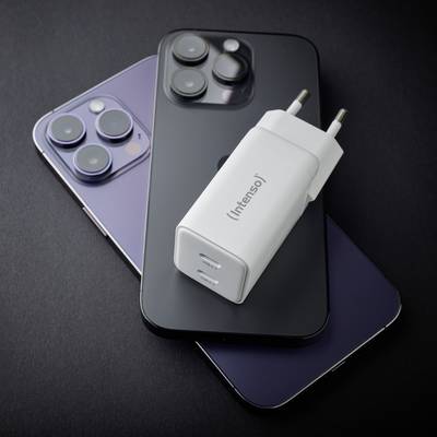 Twee smartphones met drie cameralenzen, een in paars en een in zwart, liggen over elkaar heen. Een wit oplaadapparaat ligt bovenop.