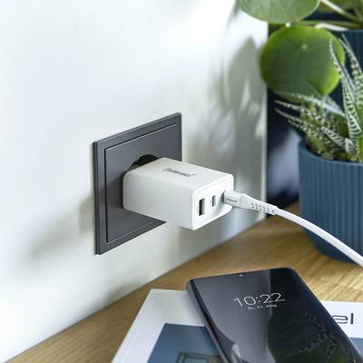 Een smartphone wordt via een oplader opgeladen aan een stopcontact. Ernaast staat een bloempot.
