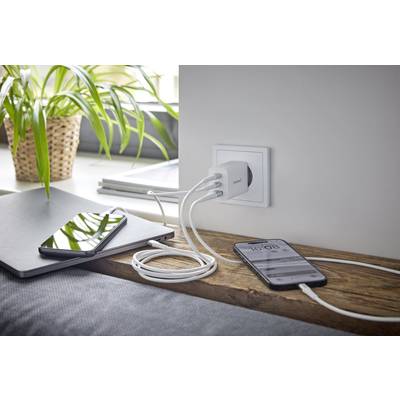 Een mobiele telefoon en laptop worden opgeladen via een stekkerdoos. Planten en boeken op de vensterbank op de achtergrond.