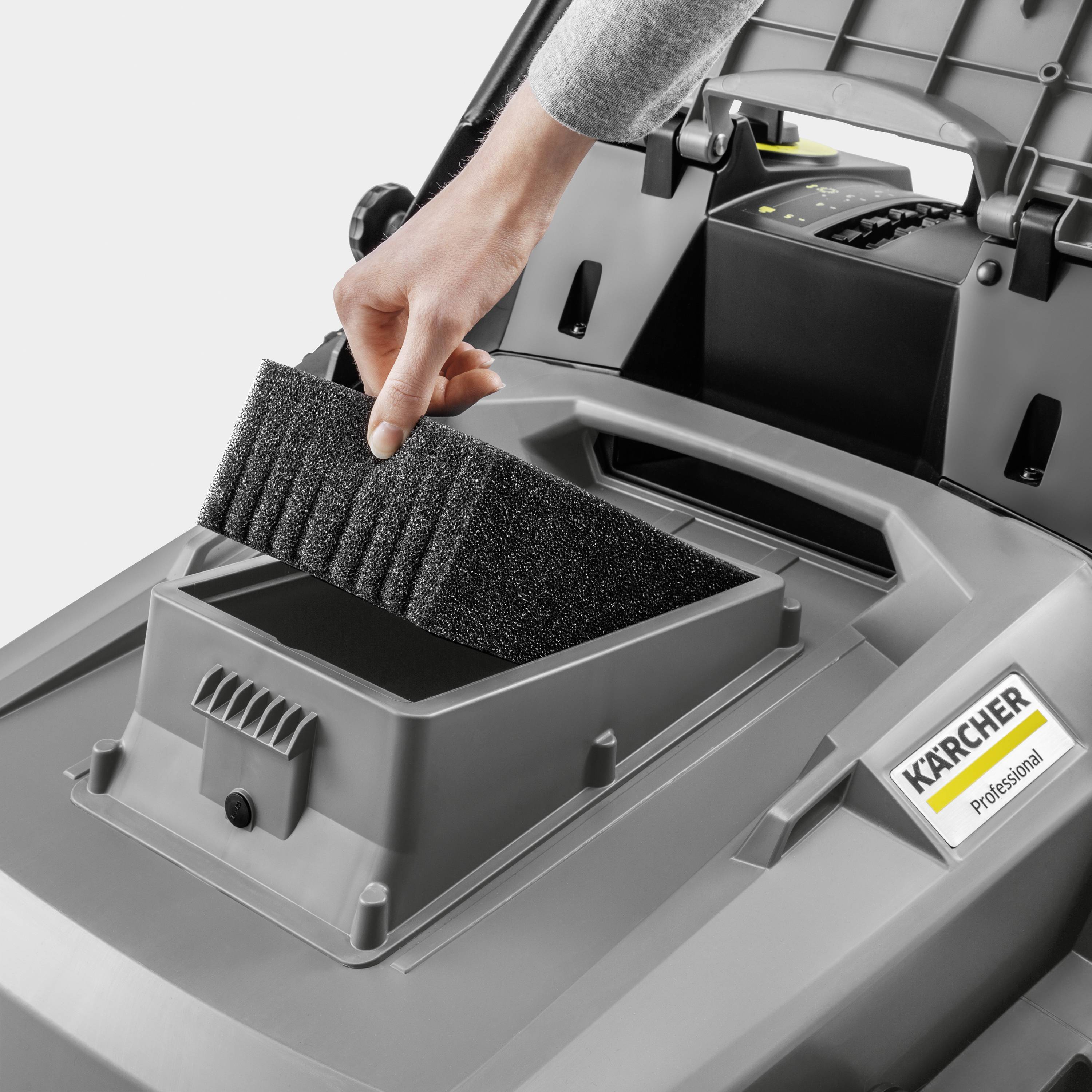 Een persoon vervangt het luchtfilter in een Kärcher reinigingsapparaat. Het apparaat staat open, en het filter wordt in de daarvoor bestemde houder geplaatst.