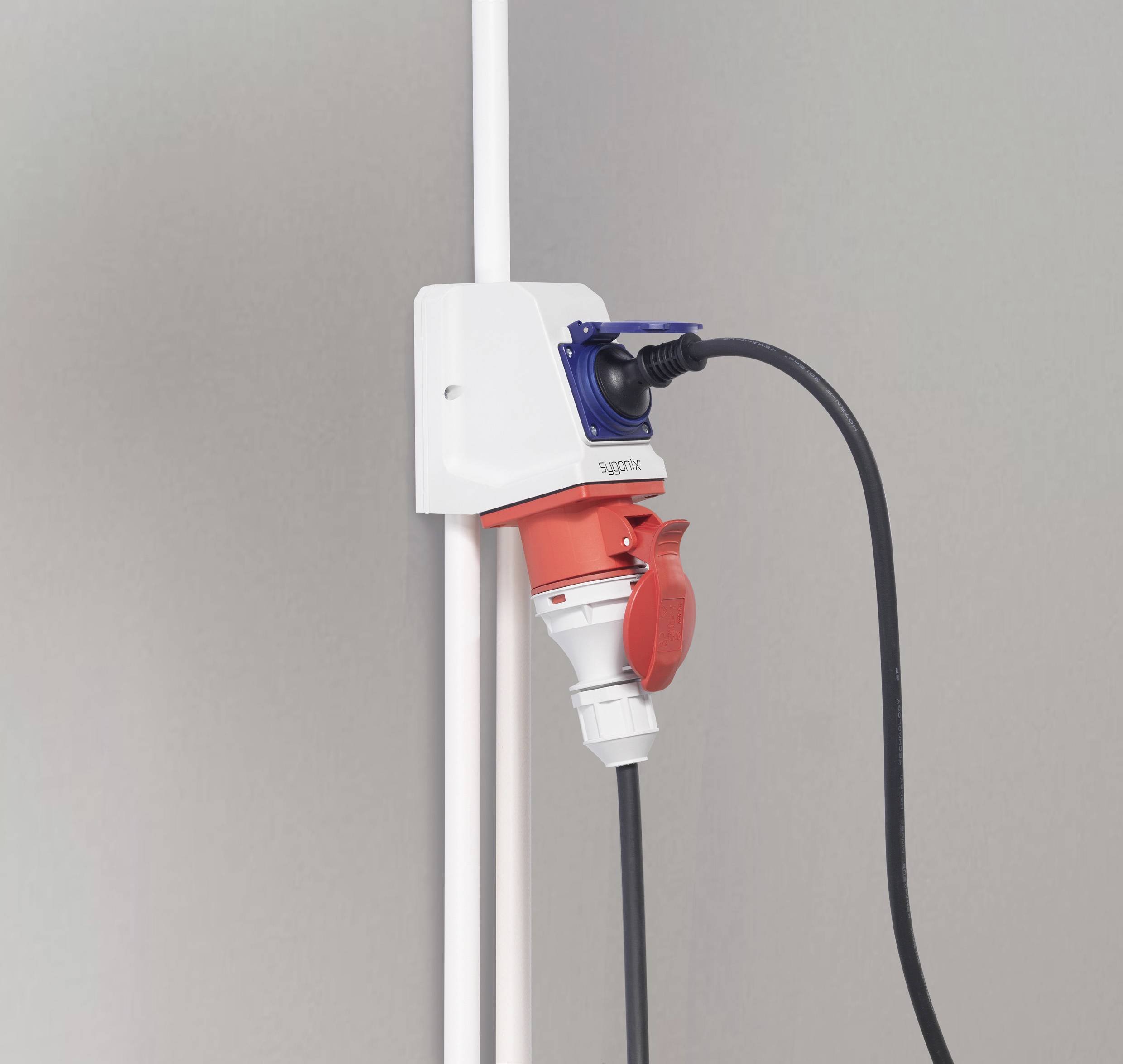 Industriële contactdoos aan de muur met een rode stekker erin gestoken. Naast de contactdoos loopt verticaal een wit snoer.