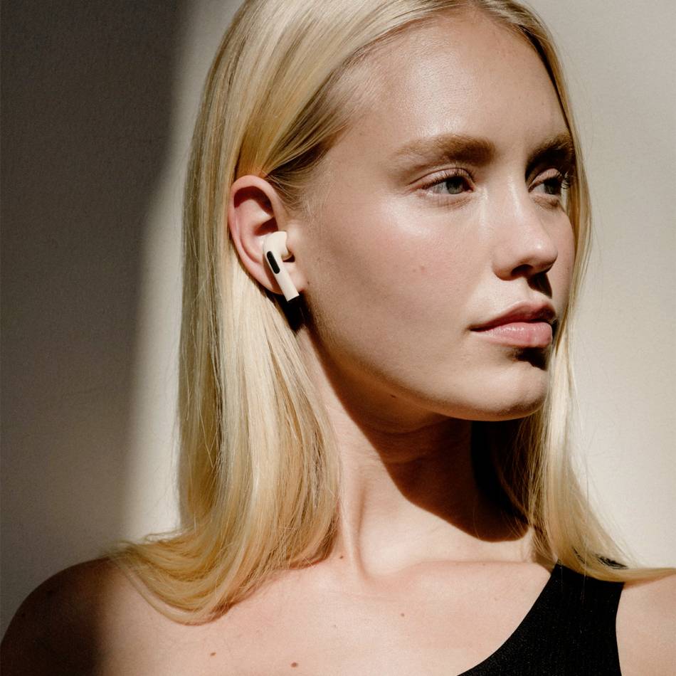 Een persoon met lang blond haar draagt draadloze oordopjes en kijkt opzij.