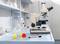 Laboratoriumwerkplek met microscoop, maatkolf en markeerstift op een laboratoriumtafel. Rek met reageerbuizen op de achtergrond.