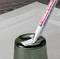 Een witte stift met de opdruk 'edding 8400 Label Remover' verwijdert een etiket van een groen glazen voorwerp.