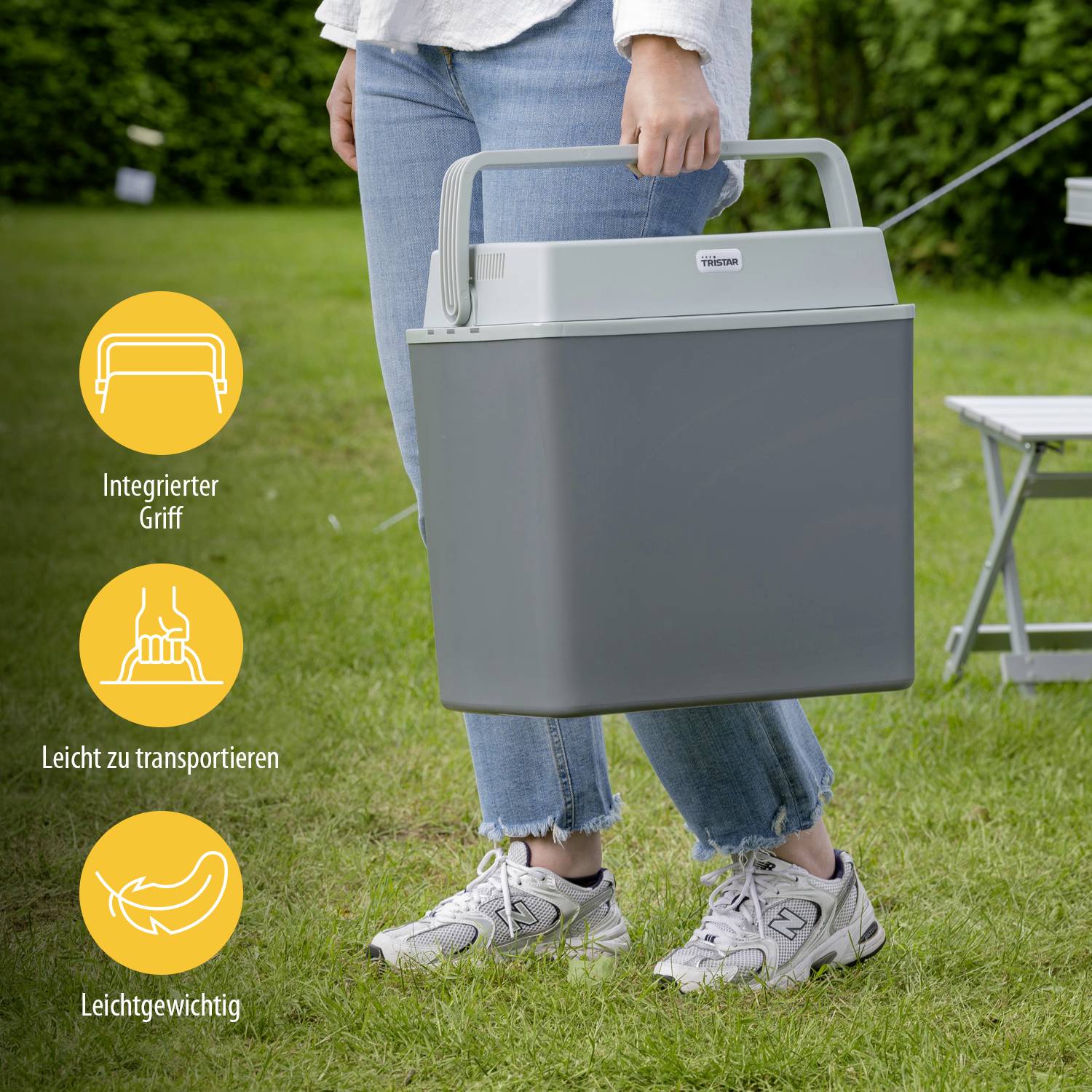 Een persoon staat op gras en houdt een draagbare, grijze koelbox met geïntegreerde handgreep. Drie symbolen tonen gebruiksvriendelijkheid: geïntegreerde handgreep, gemakkelijk te vervoeren, lichtgewicht.