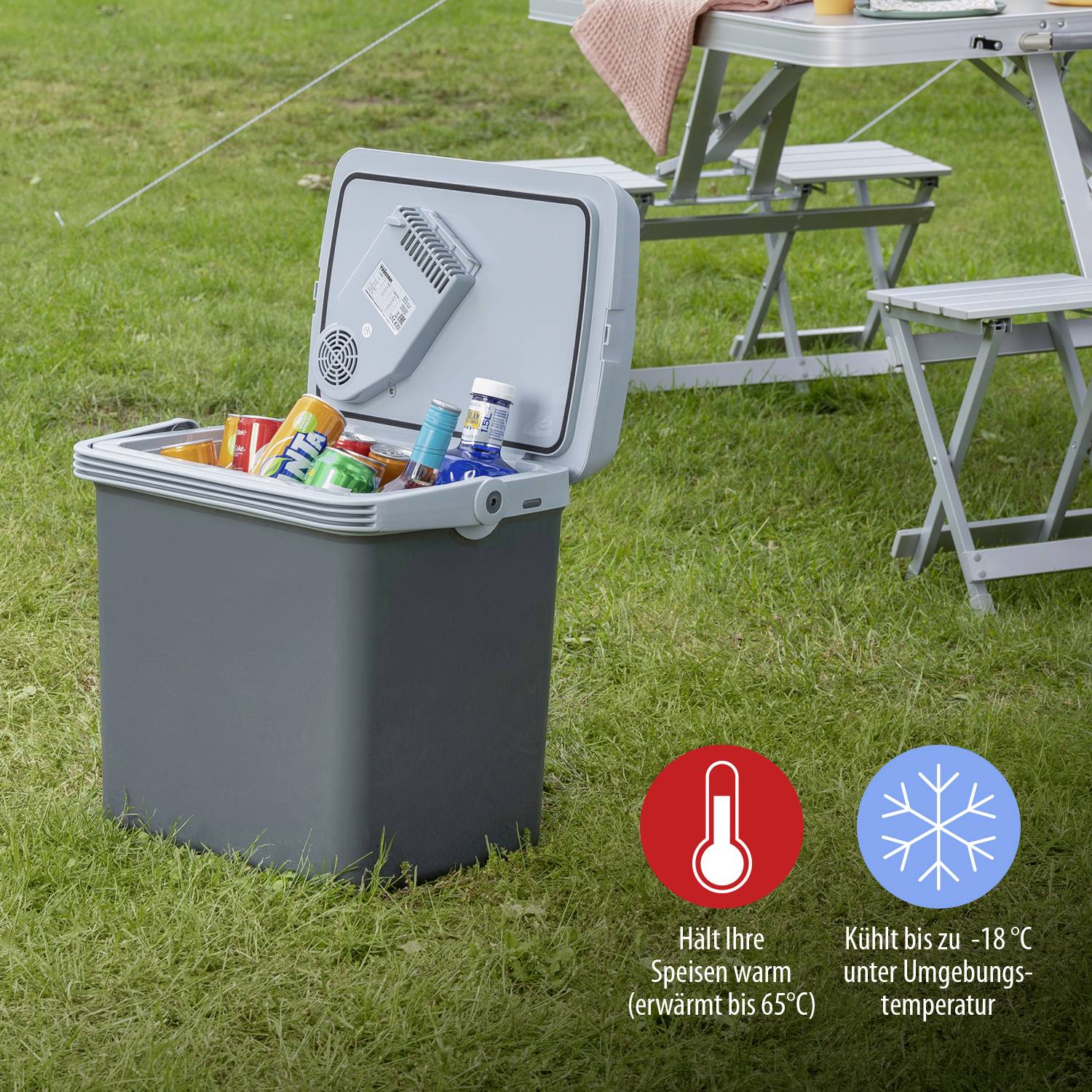 Koelbox buiten, geopend, gevuld met dranken en voedsel, geplaatst naast een campingtafel en stoelset op het gras.