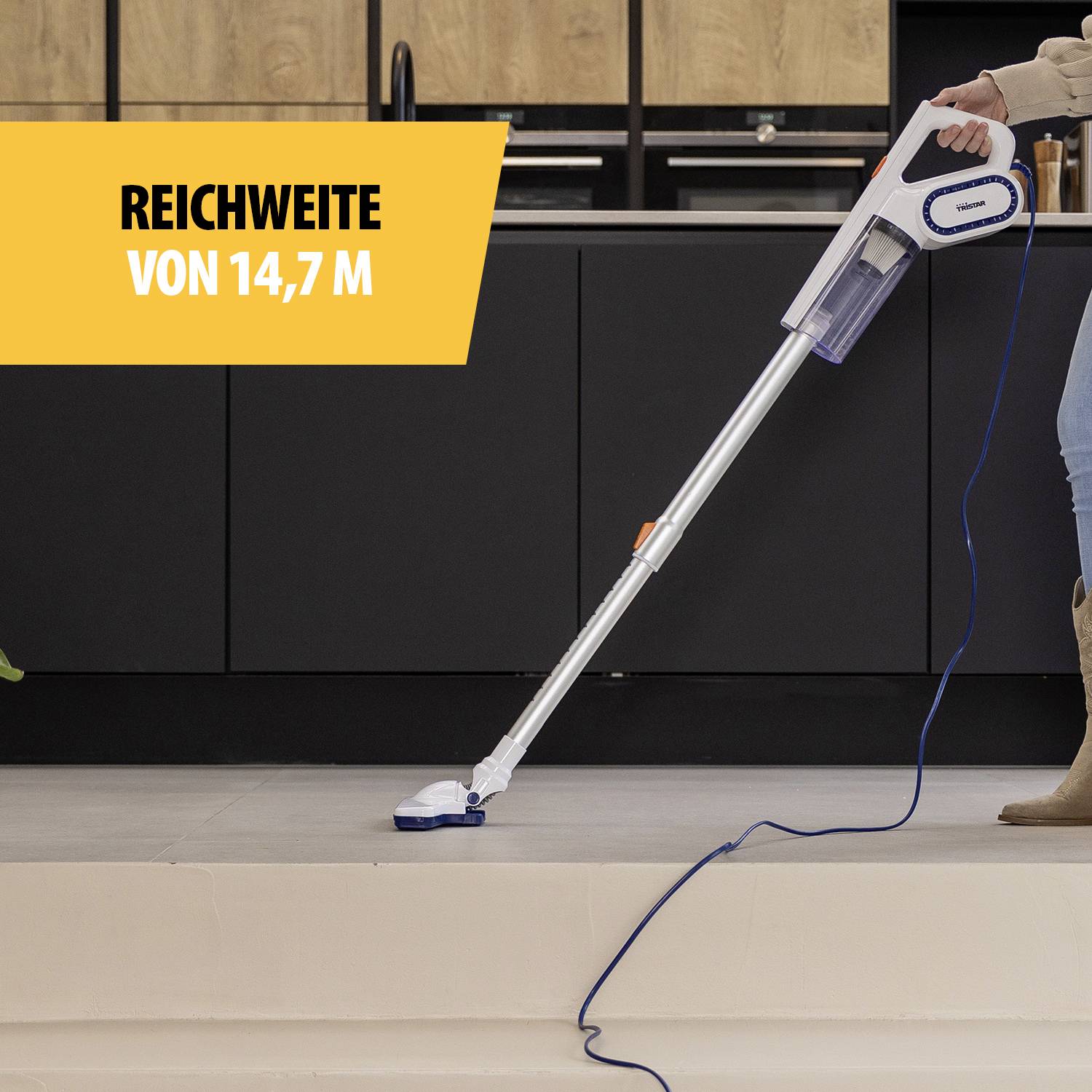 Een stofzuiger wordt door een persoon gebruikt op een lichte ondergrond. Tekst op de afbeelding: 'Bereik van 14,7 m'.