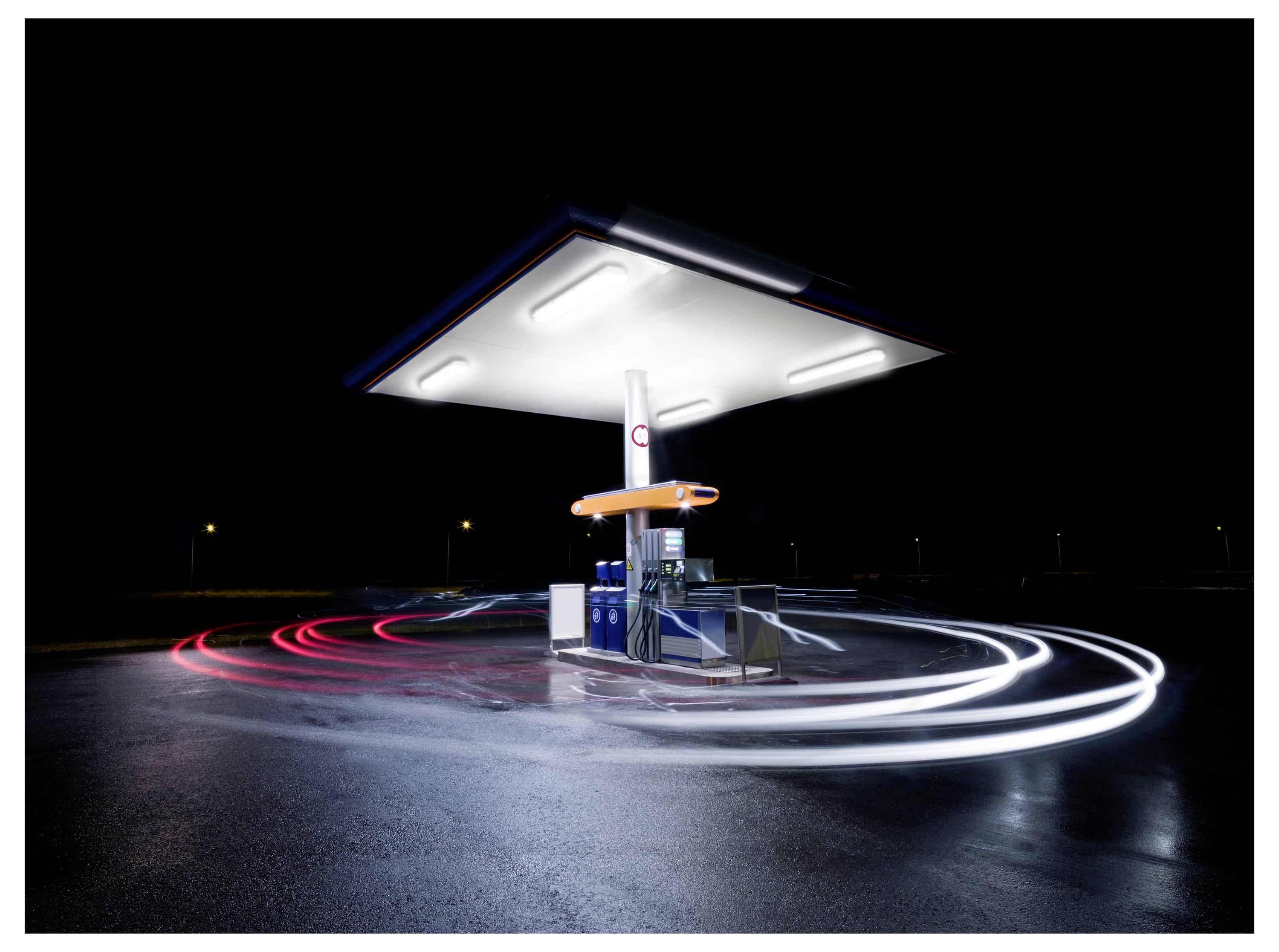 Een helder verlicht benzinestation 's nachts, geïsoleerd met vage lichtsporen eromheen, die beweging en activiteit aangeven.