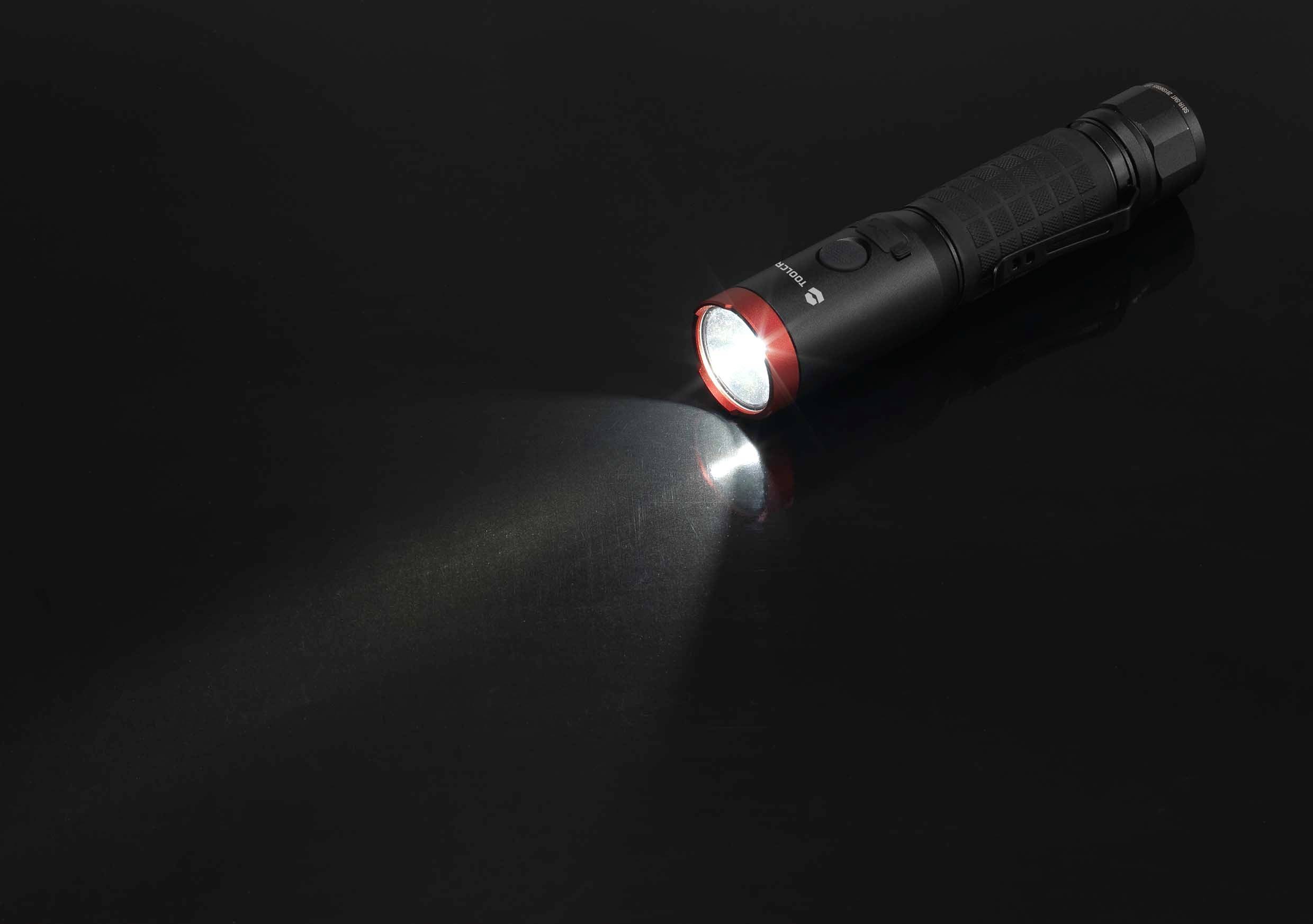 Een zwarte zaklamp ligt op een donker oppervlak en schijnt met een witte lichtstraal naar links.