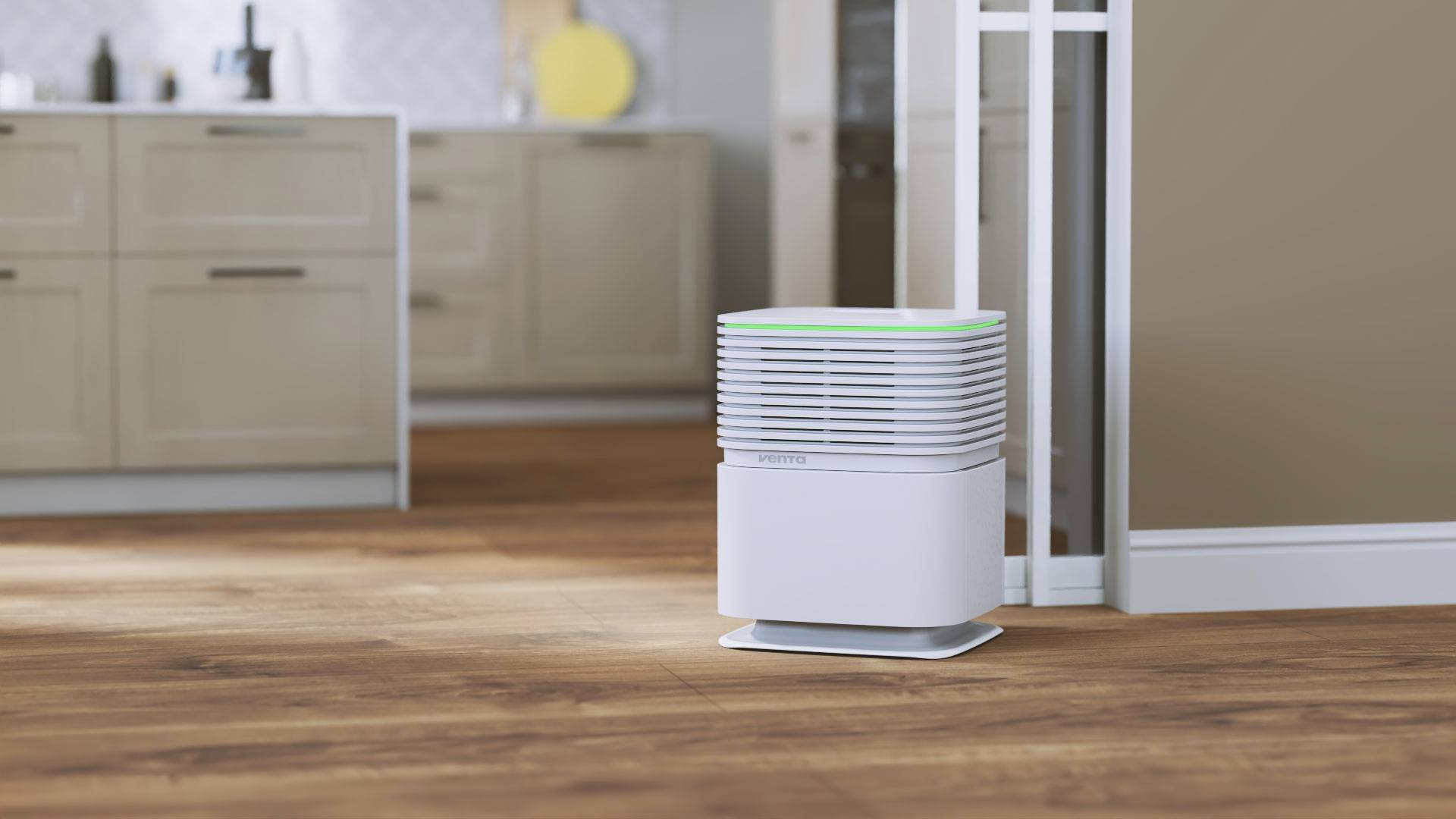 Een witte luchtreiniger staat op een houten vloer in een moderne keukenruimte. Het apparaat toont bovenaan een groen licht.