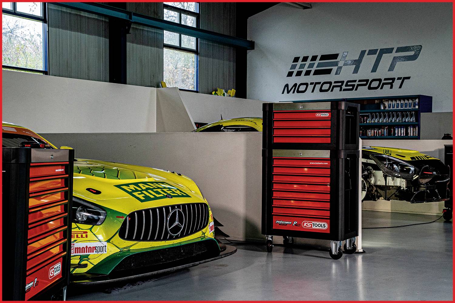 Een racewagen met het opschrift 'MANN-FILTER' staat geparkeerd in een professionele werkplaats met gereedschapswagens en het HTP Motorsport-logo.