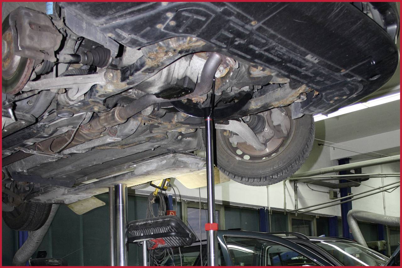 Een auto wordt op een hefbrug omhoog getild. De onderkant van de auto is zichtbaar, en er staat een montagegereedschap eronder voor onderhoud.