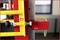 Close-up van een geel veiligheidshek en een rood apparaat aan een industriële machine die een schroef- en veerconstructie laat zien.