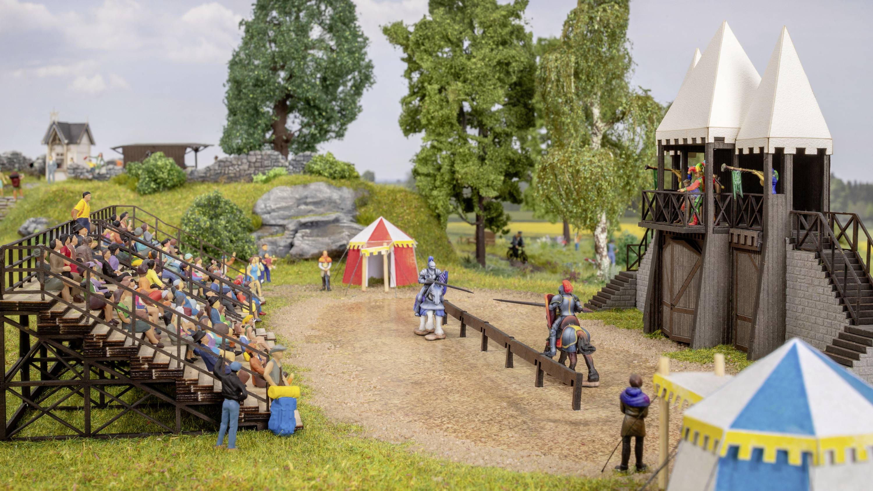 'Riddertoernooi-scène in miniatuur: Twee ridders te paard strijden op een zandarena, omringd door publiek op tribunes en in tenten.'