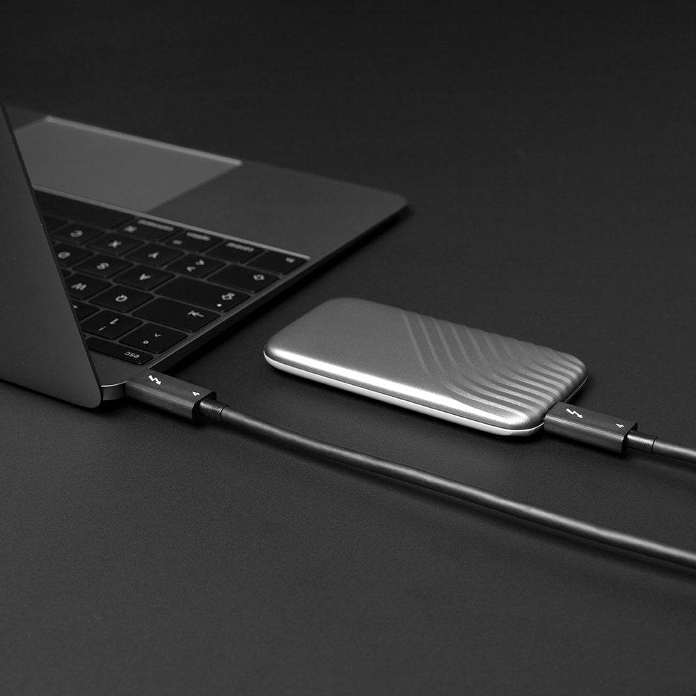 Een laptop is via een kabel verbonden met een externe zilveren harde schijf die op een tafel ligt.