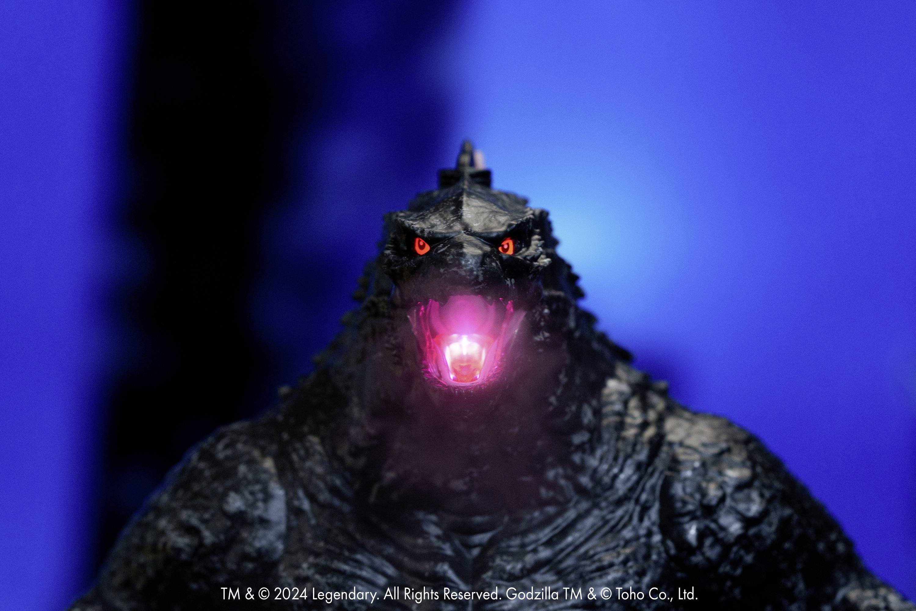 Een figuur van een gigantisch monster met lichtgevende ogen en een open, oplichtende mond voor een blauwe achtergrond.