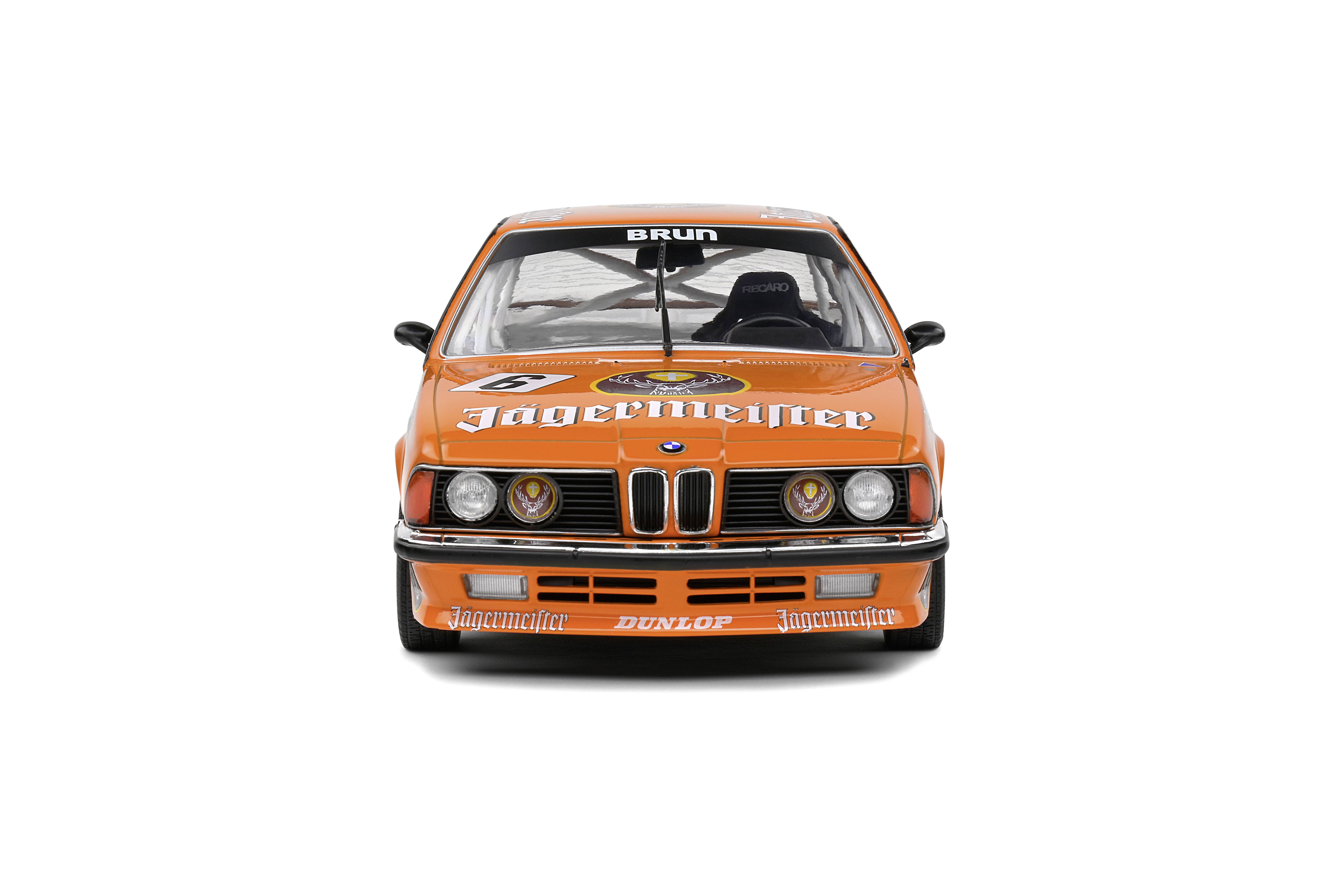 Een oranje racewagen met 'Jägermeister' op de motorkap, vooraanzicht, met racenummer en sponsorlogo's.