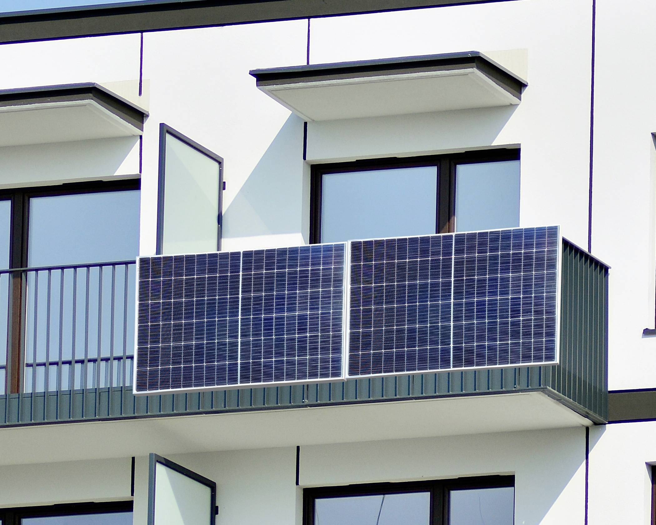 Zonnepanelen op de balustrade van een balkon van een modern woongebouw. De openslaande balkondeur wijst op gebruik of installatie.