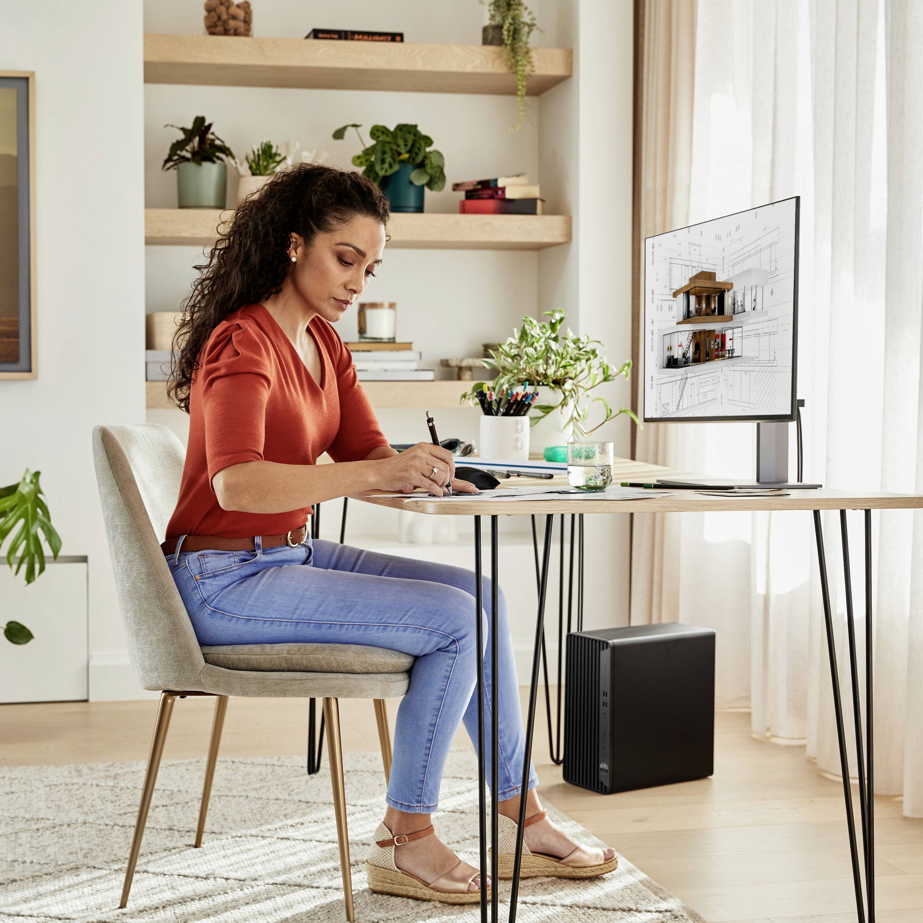 Vrouw aan haar bureau werkt geconcentreerd aan documenten, terwijl een computer een architectonisch ontwerp toont. Lichte, moderne omgeving.
