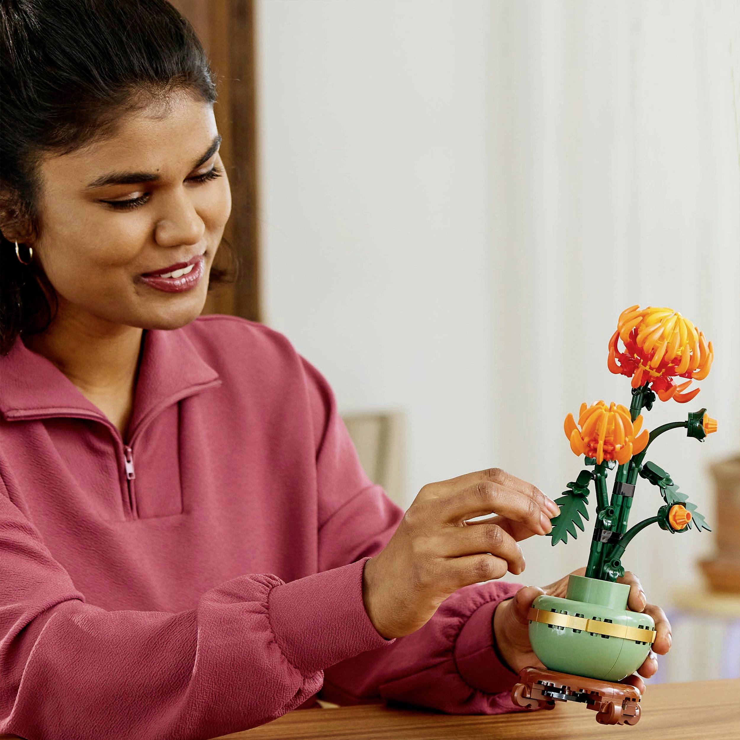 Een persoon in een rode trui bekijkt een gemodelleerde oranje bloem in een kleine pot.