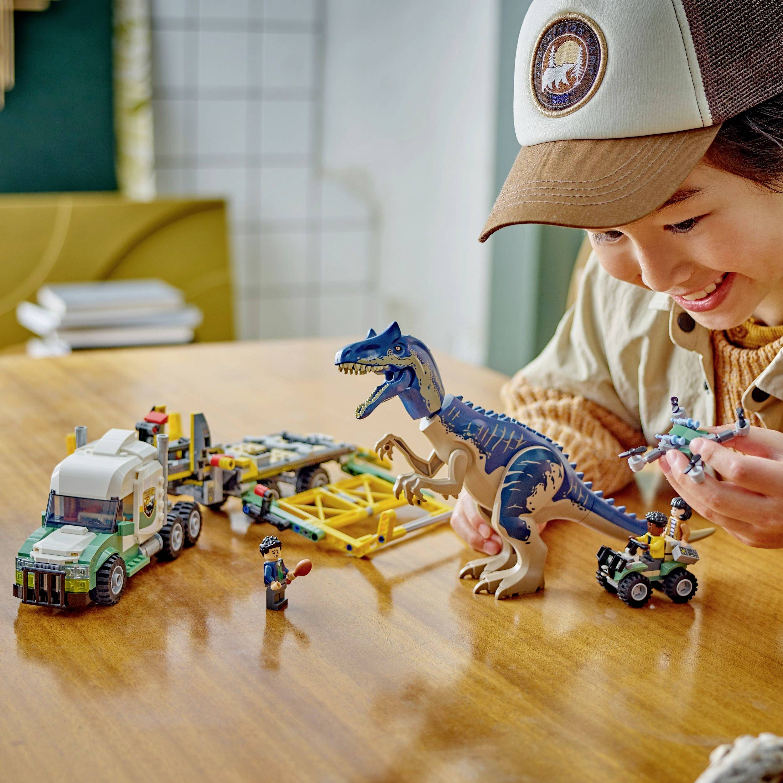 Een kind speelt met een dinosaurus- en een vrachtwagenspeelgoed op een tafel. Op de achtergrond is een bank zichtbaar.