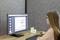 Een vrouw zit aan een bureau en bestudeert een diagram op een computerscherm. Op de achtergrond bevindt zich een grijze scheidingswand.