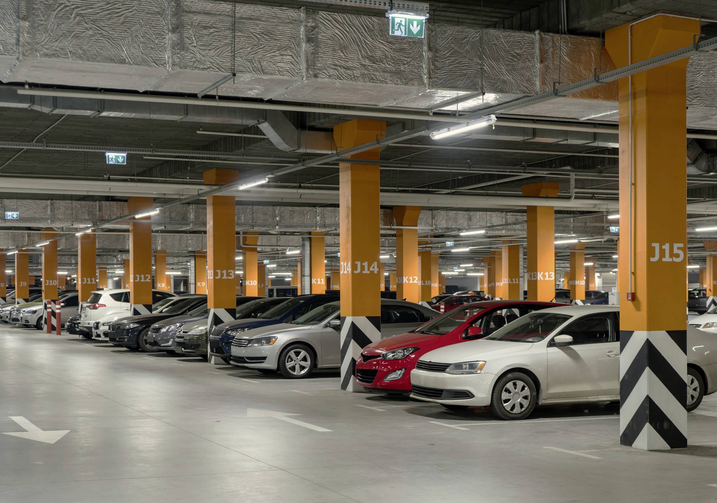 Een ruime, goed verlichte parkeerzone in een parkeergarage. Verschillende auto's staan naast elkaar geparkeerd tussen oranje gemarkeerde zuilen.