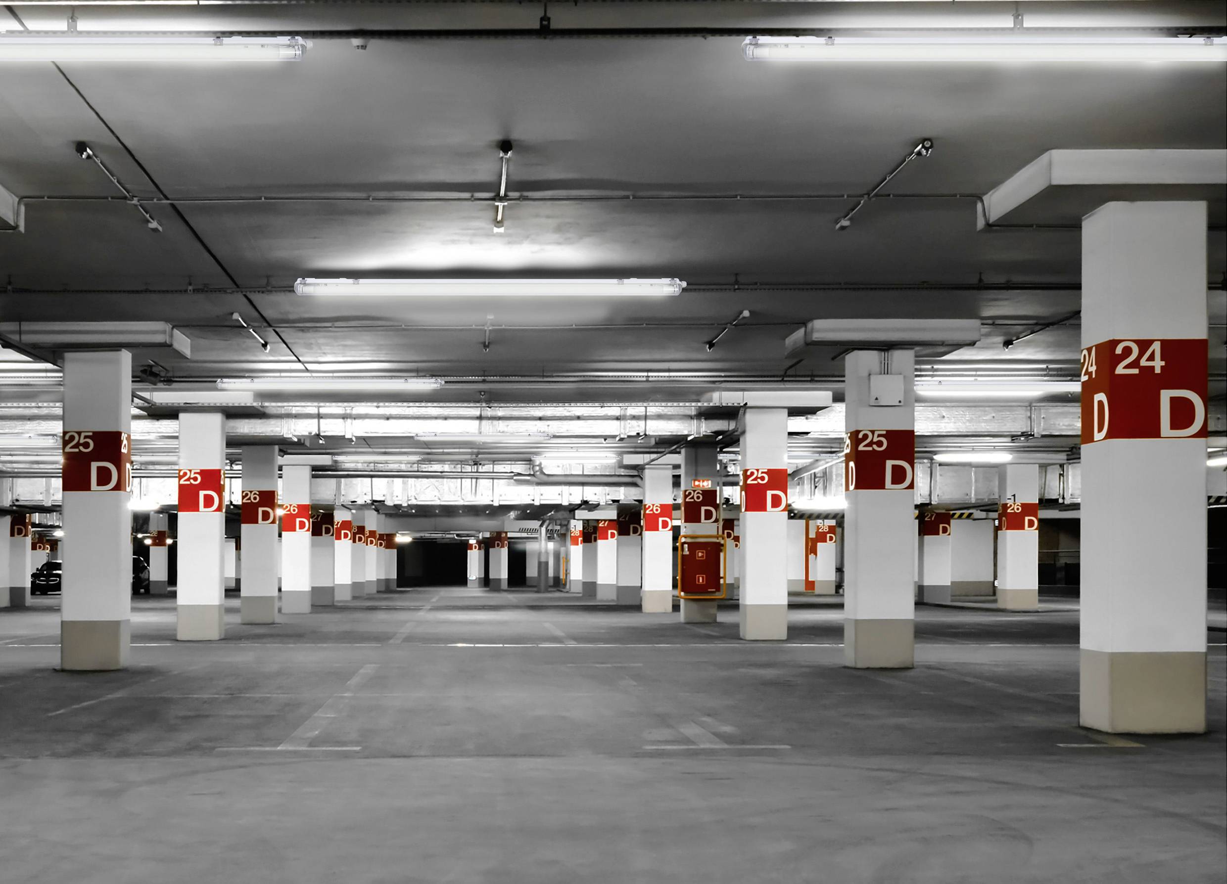 Een lege, verlichte parkeergarageruimte met zuilen die gemarkeerd zijn met letters en cijfers, bijvoorbeeld 'D24' en 'D25'.