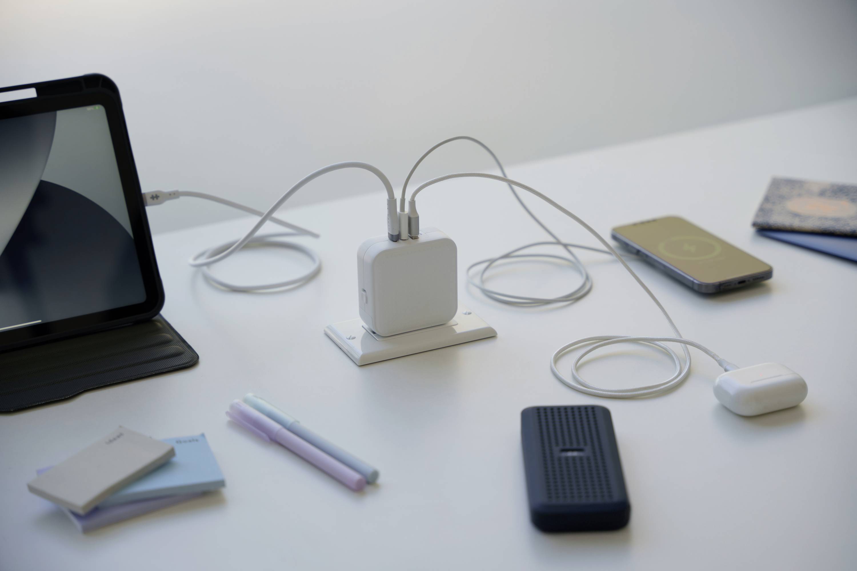 Tablet en smartphone op een tafel, verbonden met een oplader. De oplader laadt meerdere apparaten tegelijkertijd op.