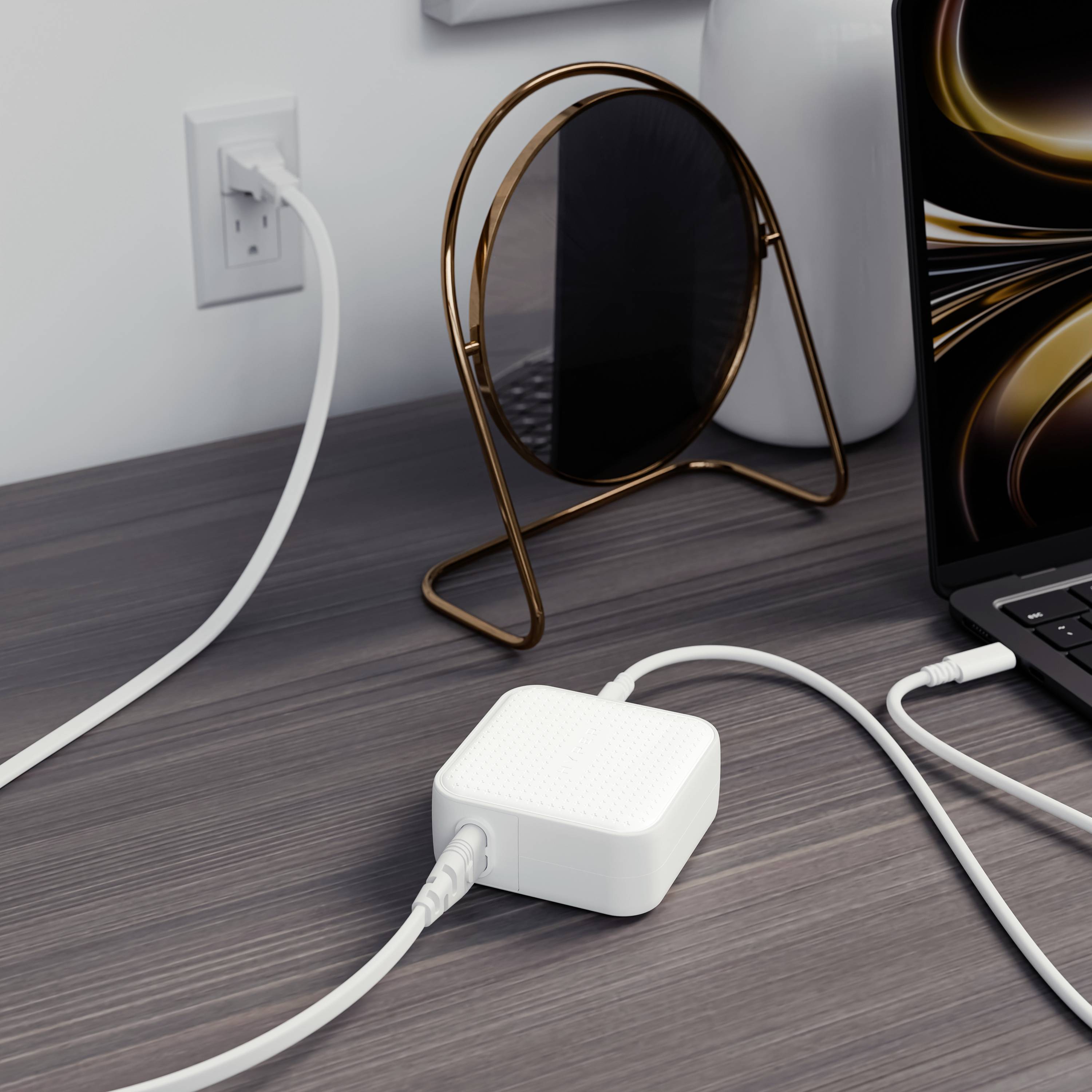 Een witte adapter is aangesloten op een stopcontact. Een smartphone-kabel is erin gestoken. Op de achtergrond is een laptop zichtbaar.